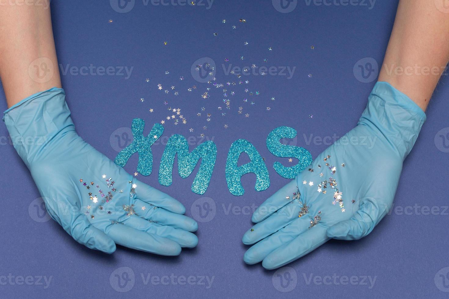 Hands in medical gloves on blue background. Glitter little stars in hands. Inscription XMAS. Christmas and New Year card concept. Top view photo, copy space. High quality photo