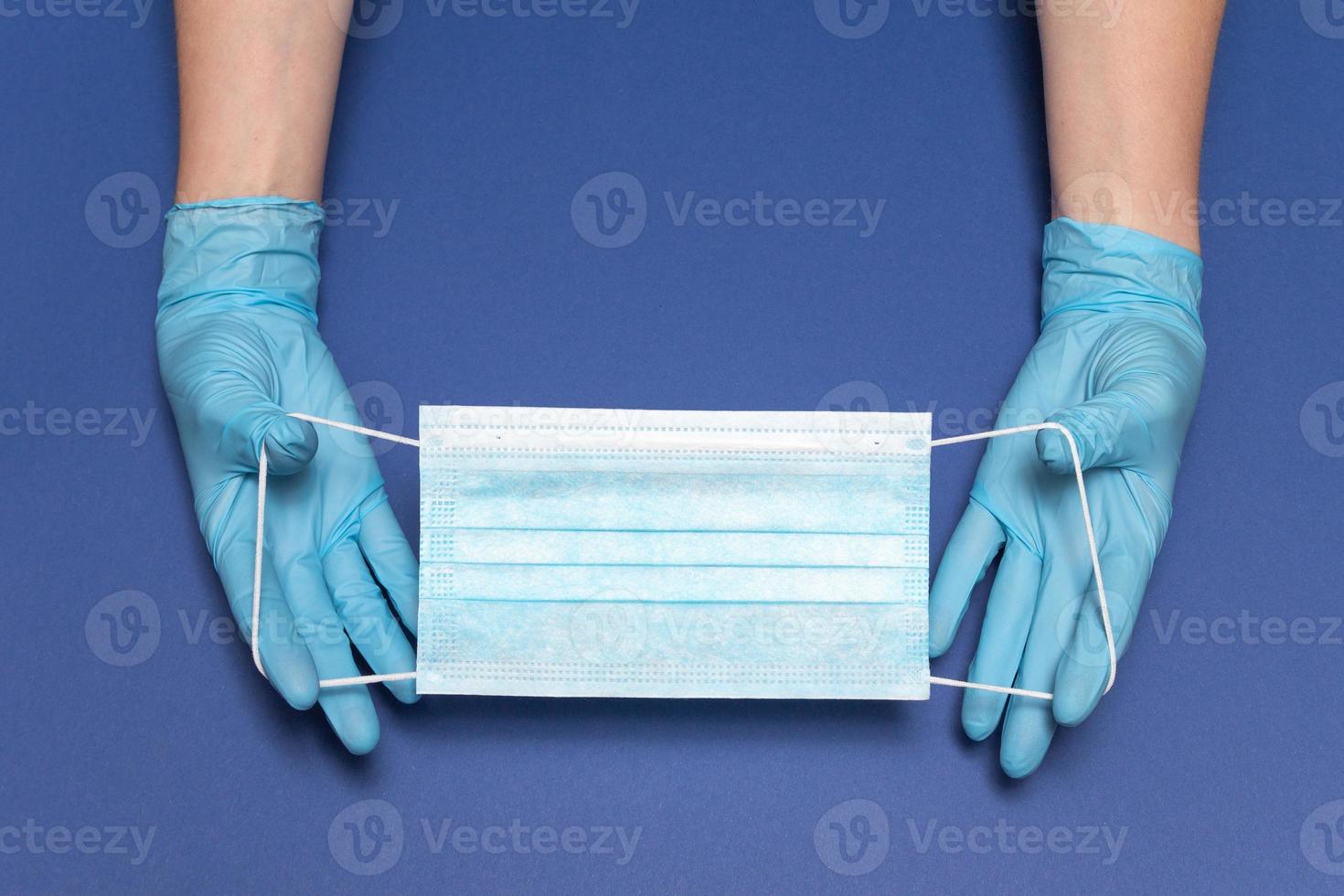 Hands in blue medical gloves is holding face mask on blue background. Protective respiratory medical mask against spreading virus. Close up, copy space, top view, flat lay. High quality photo