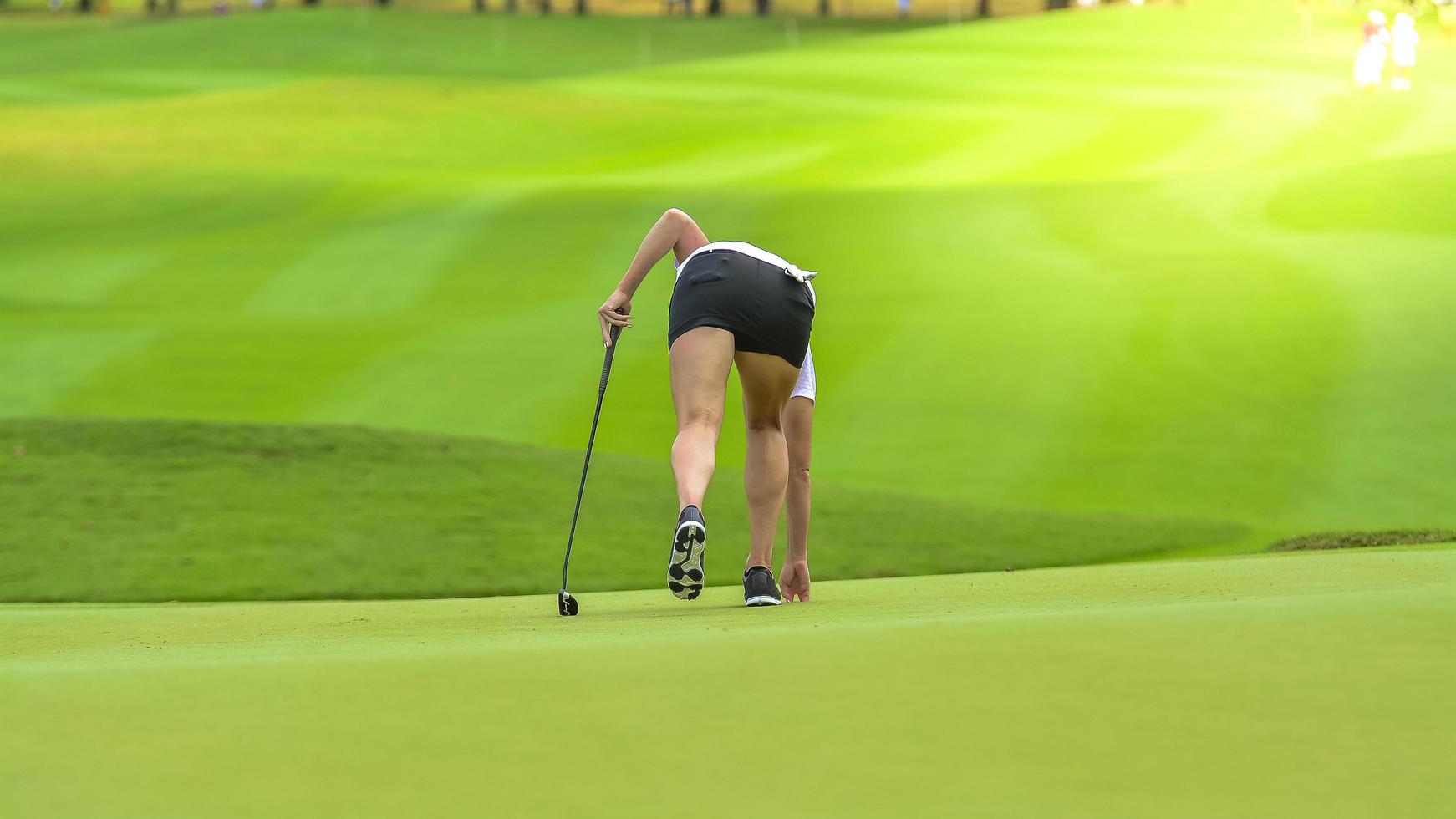 Golfer pushing white golf ball to hole at golf course in golf competition game , sunlight rays and blur background in golf tournament photo