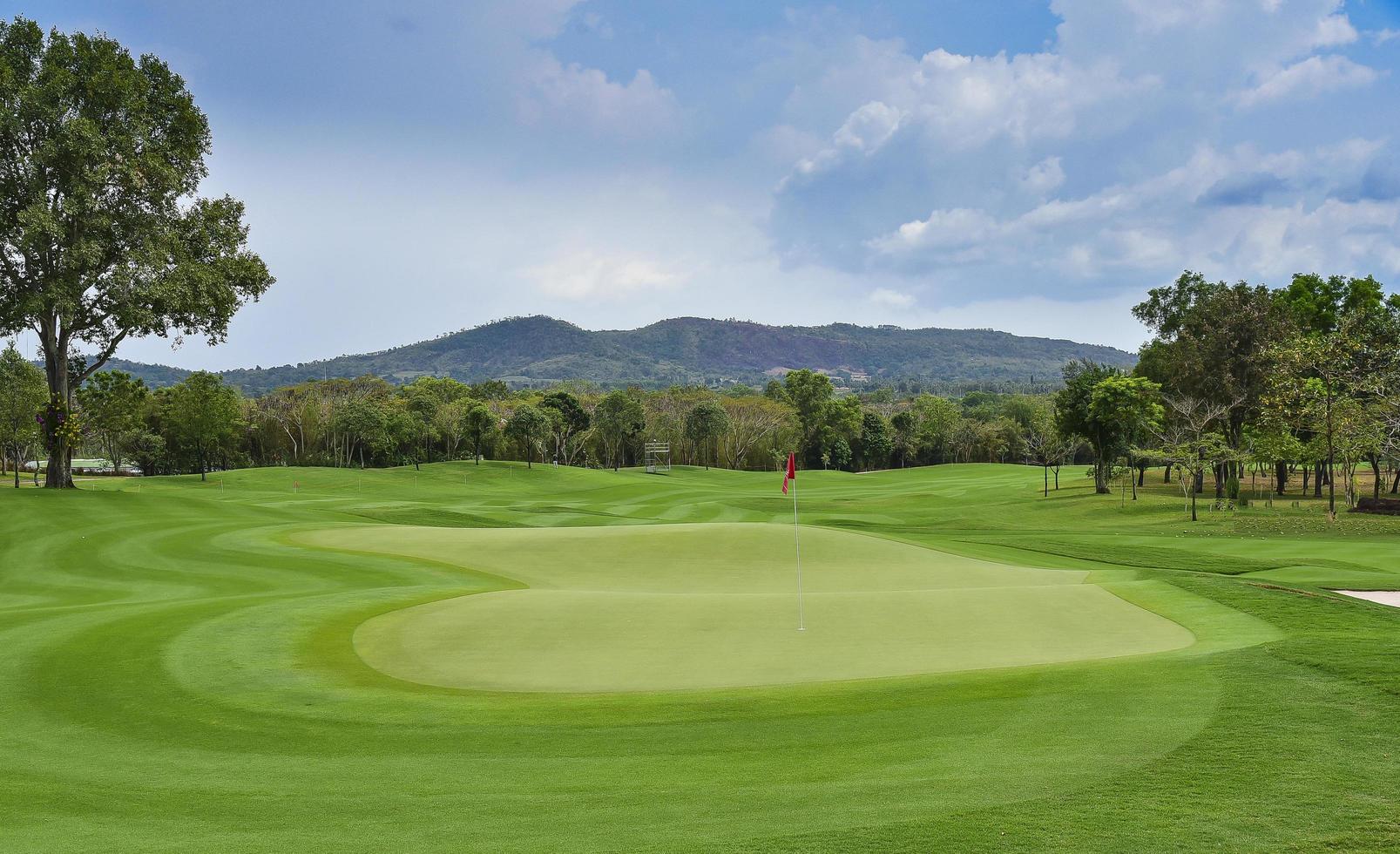 una vista del paisaje de hierba verde en el campo de golf, árboles grandes con fondo de cielo de luz solar foto