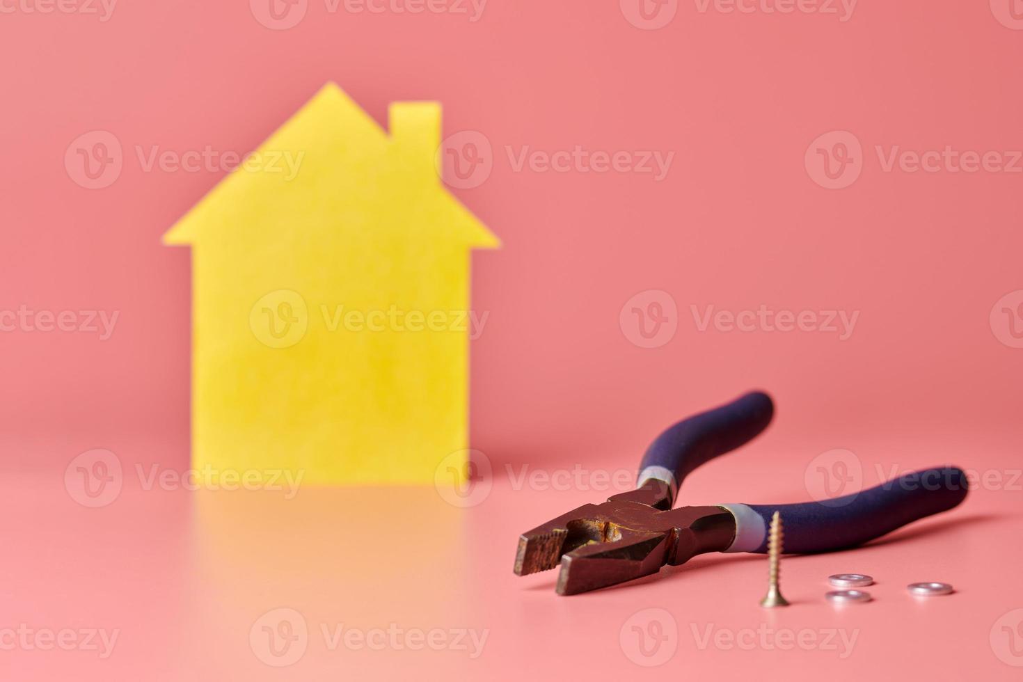 House renovation concept. Home repair and redecorated. Lineman pliers, screws and yellow house shaped figure on pink background. photo