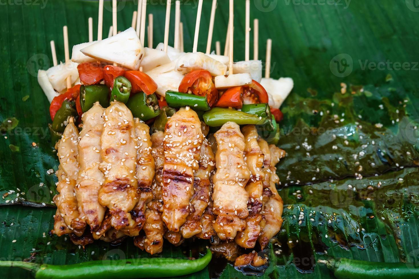 Close up Street food Grilled Chicken BBQ paste white sesame in wooden skewers with tomato pineapple pepper. Place on the tray with a green banana leaf. photo