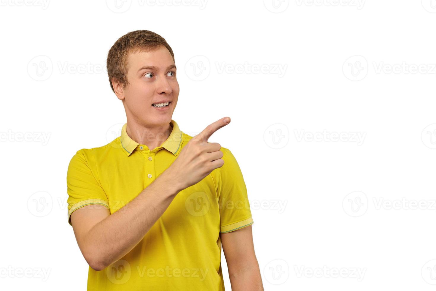 Surprised guy with funny face in bright yellow T-shirt pointing finger to right, white background photo