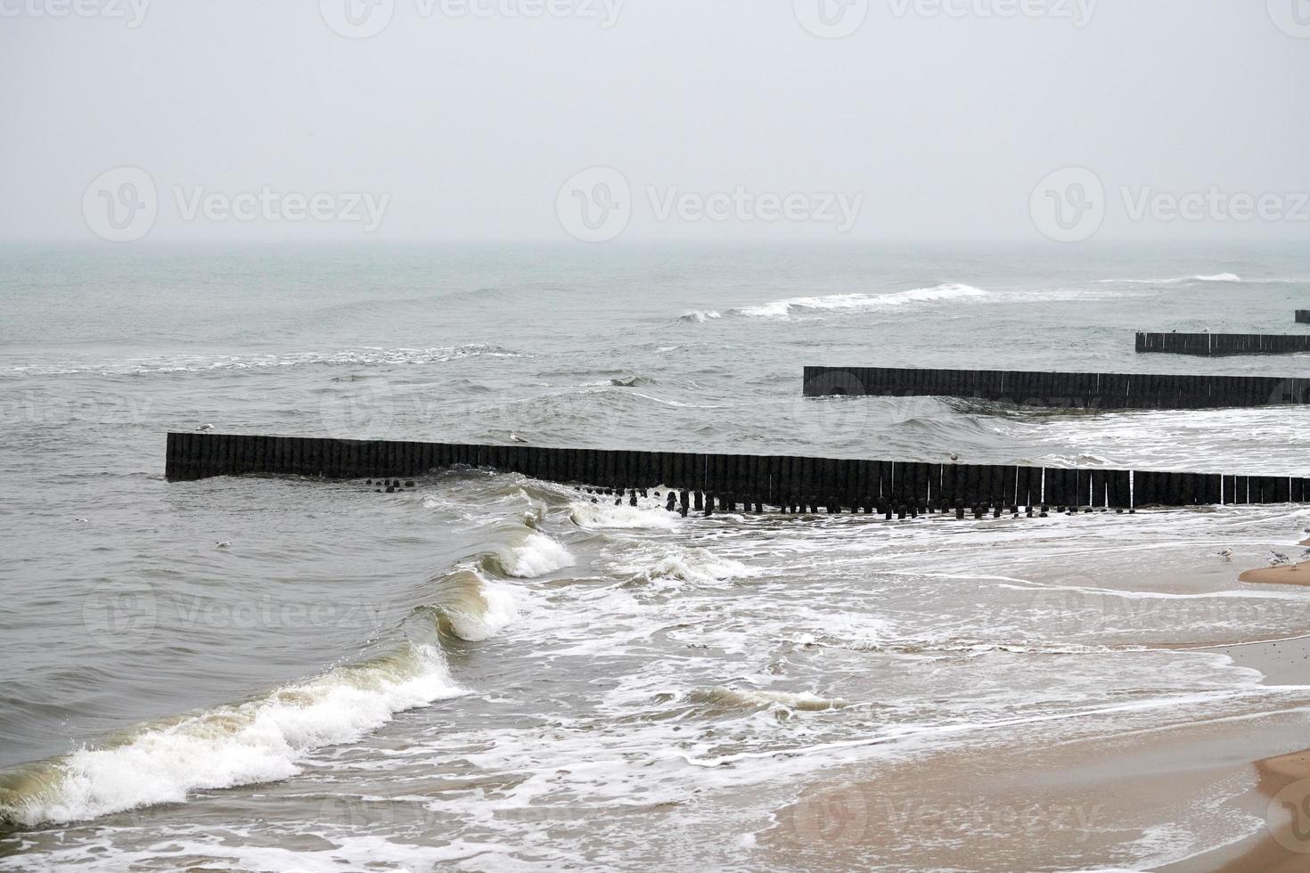 Old long wooden breakwaters in sea waves, winter landscape photo