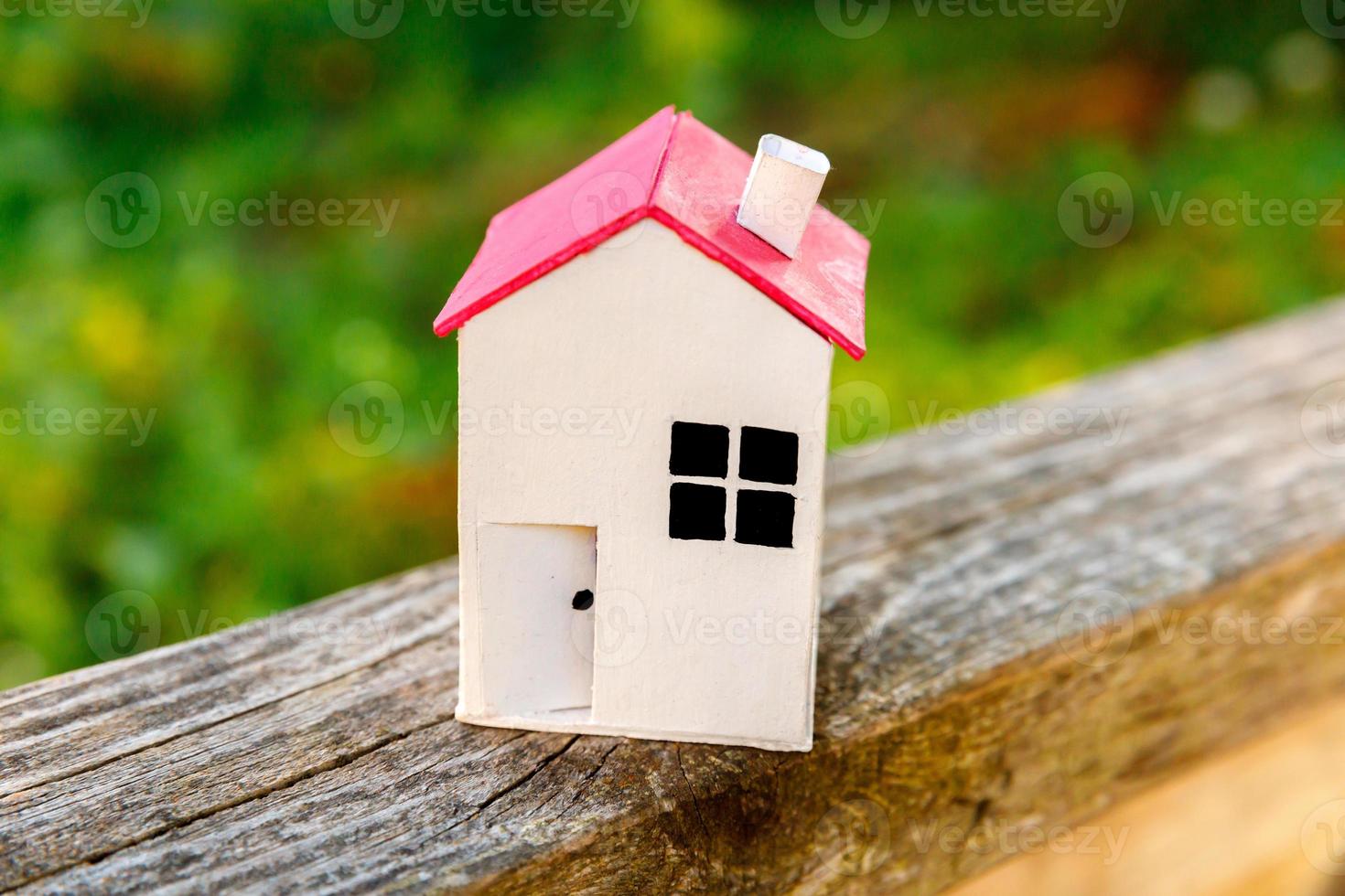 Miniature white toy model house in wooden background near green backdrop. Eco Village, abstract environmental background. Real estate mortgage property insurance dream home ecology concept. photo
