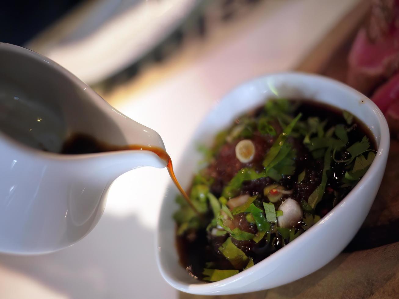 Close up selective focus of pouring japanese soy sauce from ceramic jug into ceramic  bowl photo