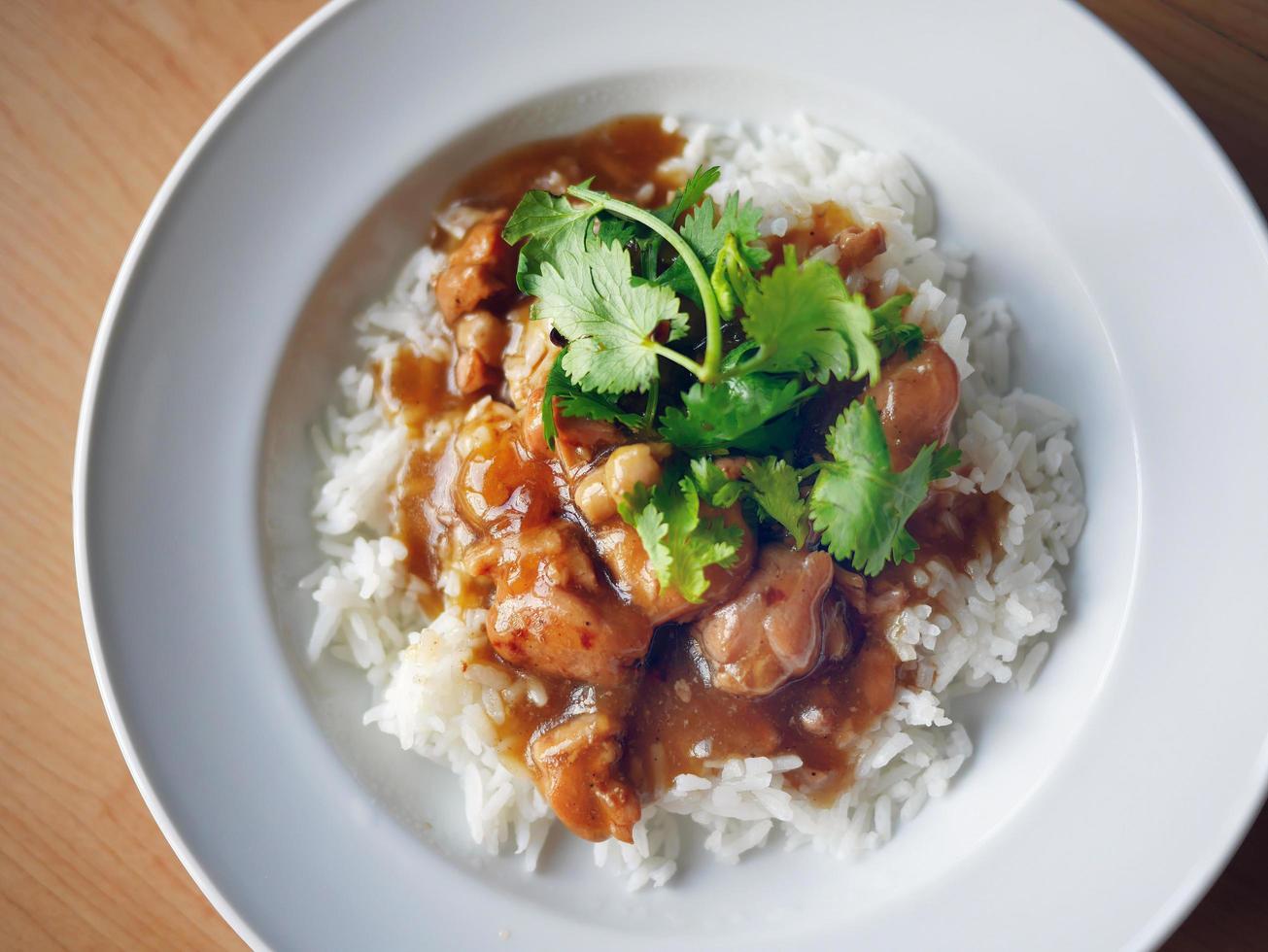 close-up chicken in brown sauce chinese style over rice cover with coriander in white plate photo