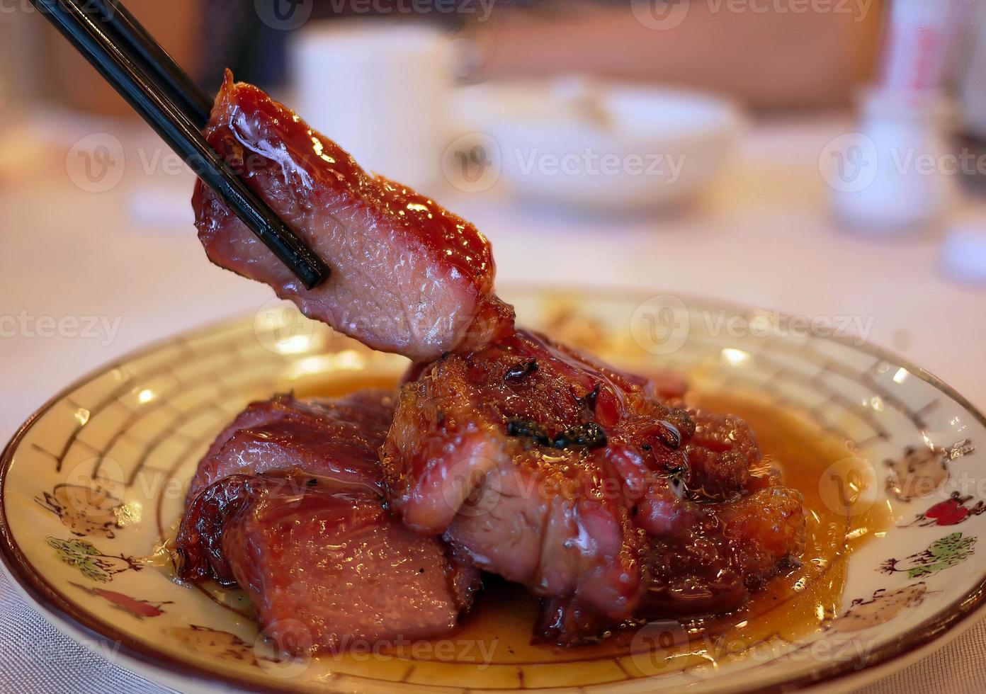 primer plano vista lateral palillos sosteniendo un pedazo de jugoso delicioso asado de cerdo asado al estilo cantonés foto