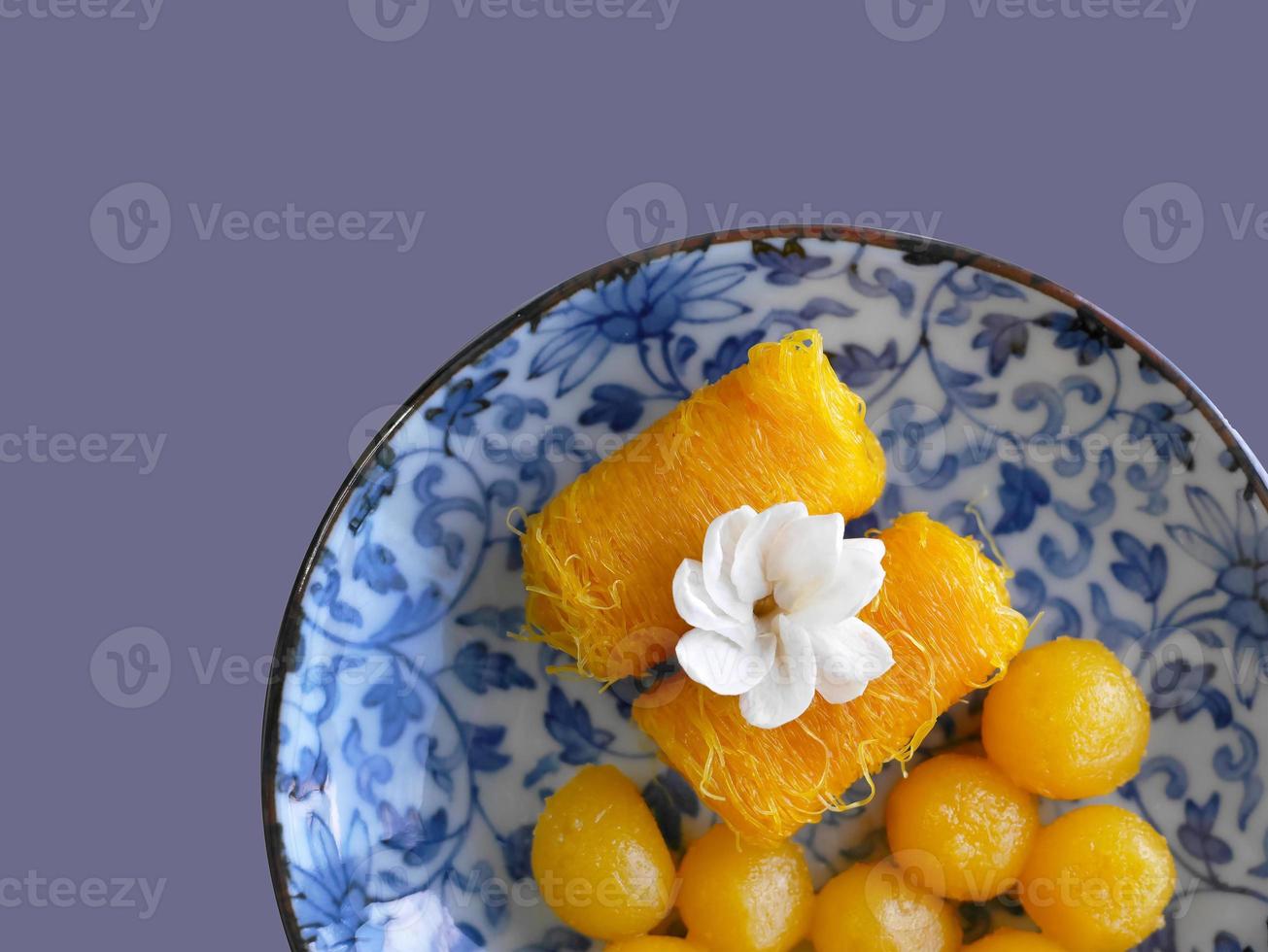 Top view, Close up of Thai style Fios de ovos, rolled golden egg yolk thread and gold egg-yolks drops, Thong yot, traditional sweet food dessert in blue painting plate, copy space with clipping path photo