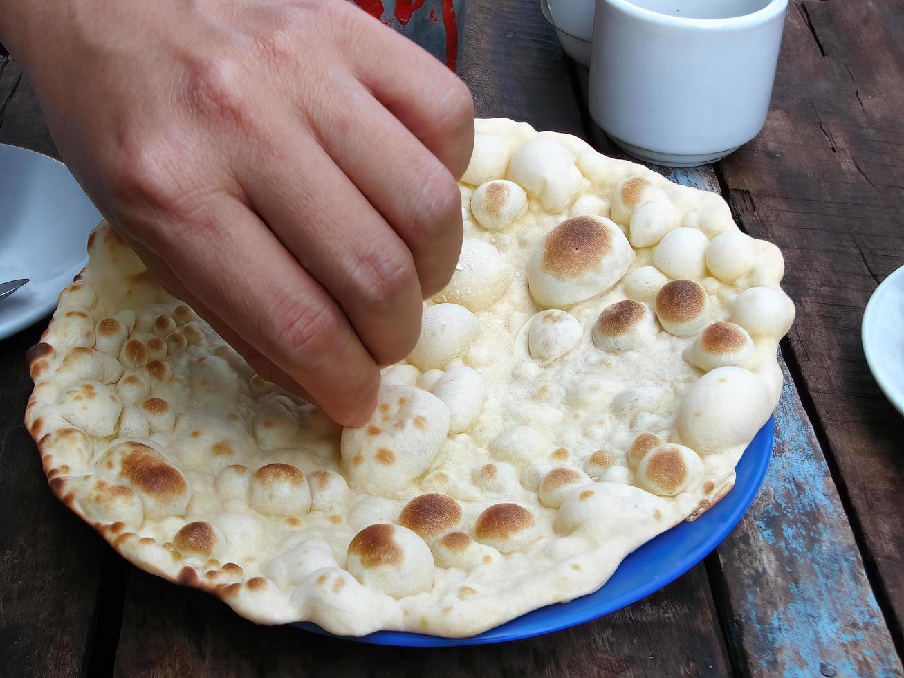 Close up of a hand picking crispy oven-baked Roti in the blue color plate, street food, in Yangon Market Myanmar. South east asia. photo