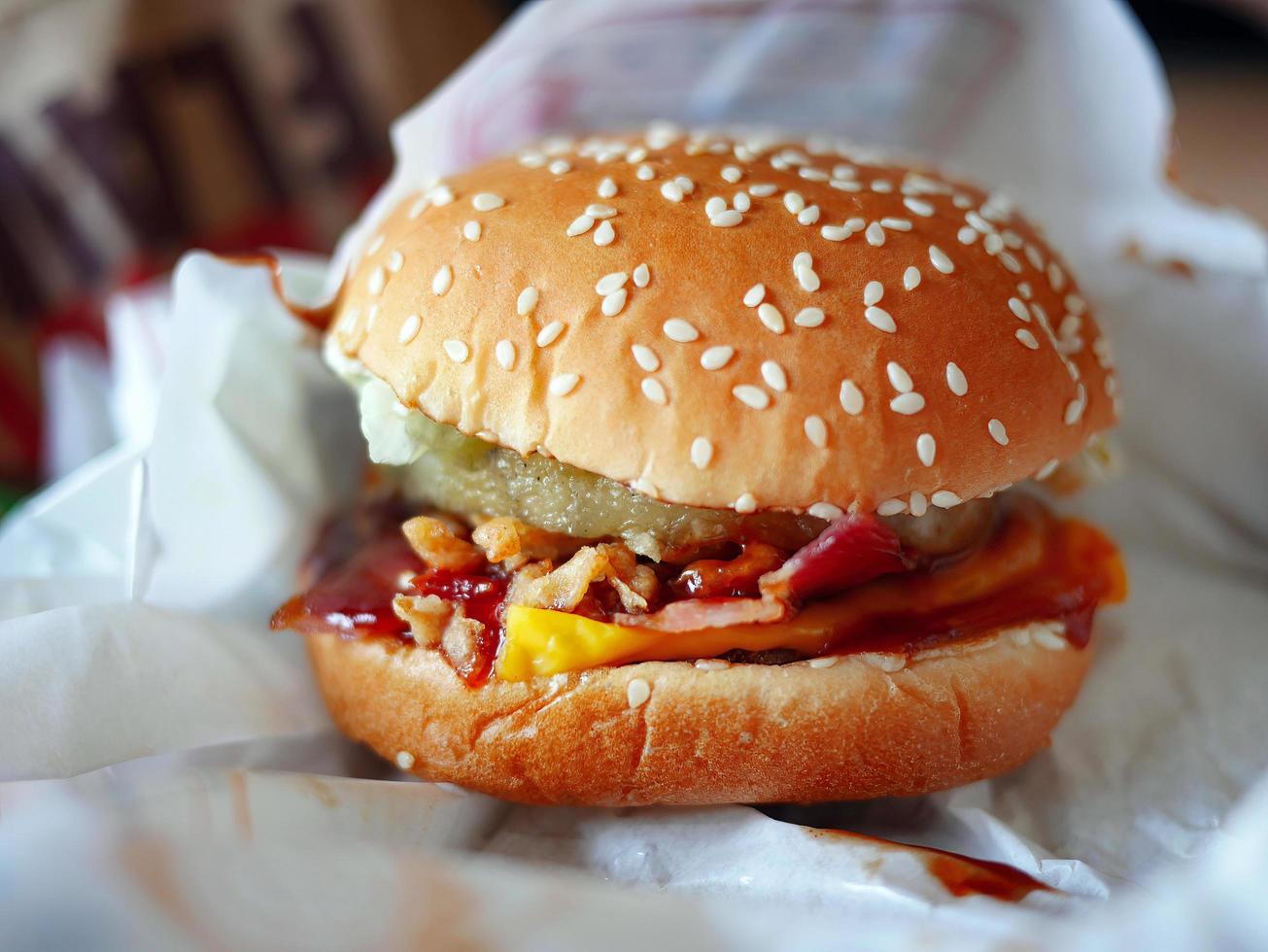 close-up Local style delicious bacon pineapple slice cheese burger sesame bun wrap by white paper photo