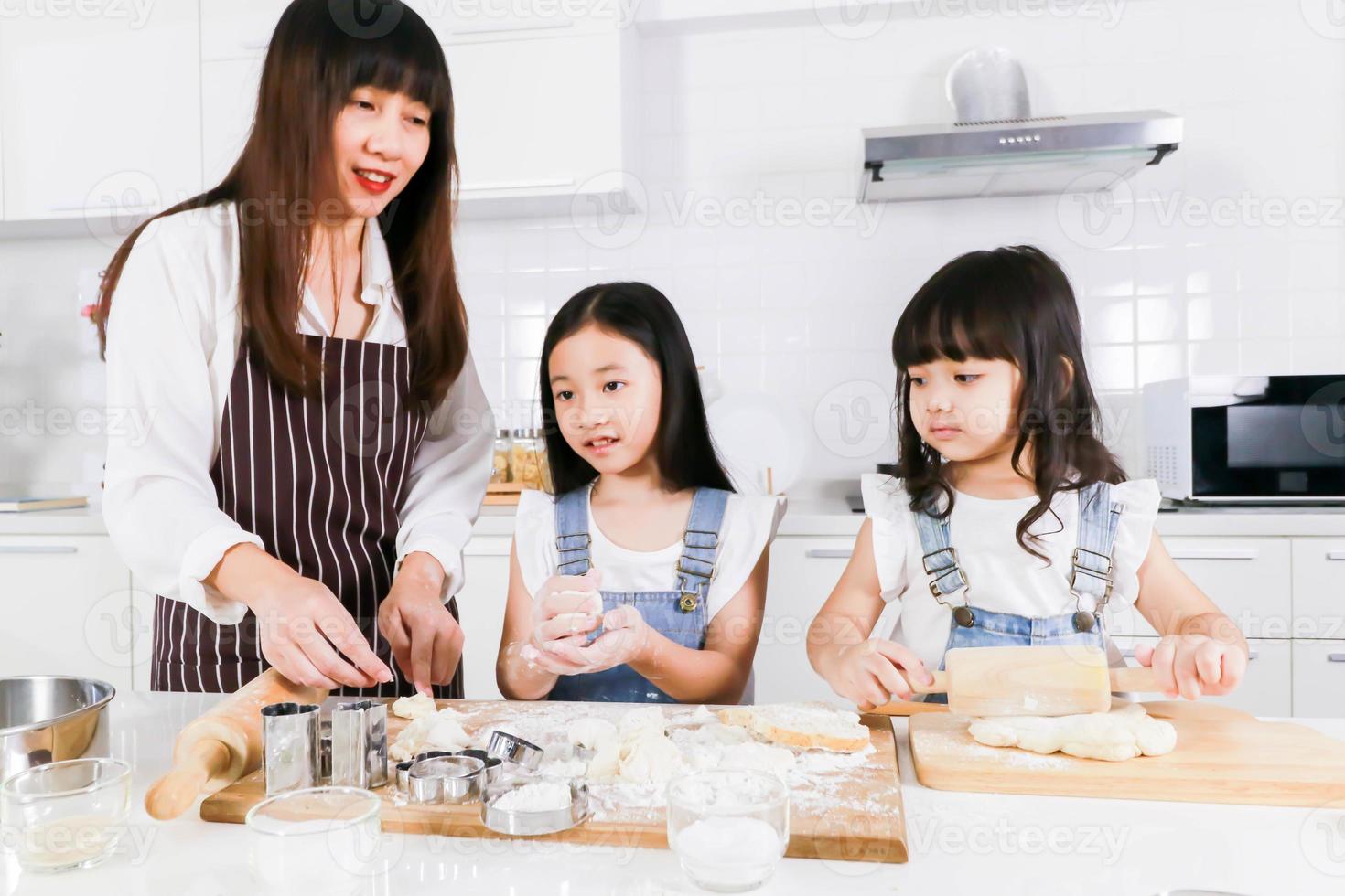 Smiling young mom teaching little daughter doing bakery at home kitchen photo