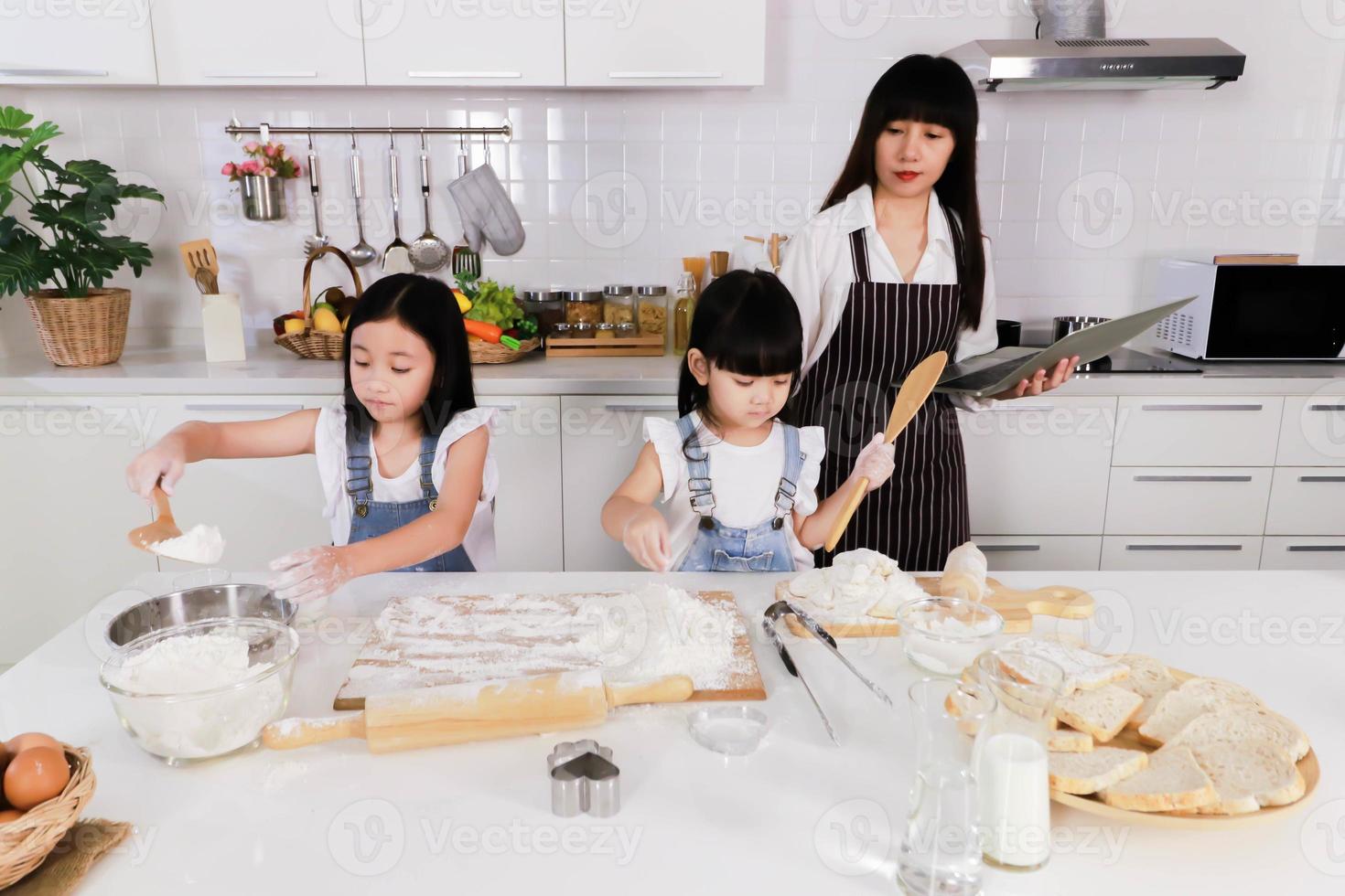 madre que mira a la hija pequeña y a la hermana pequeña hacen un horneado foto