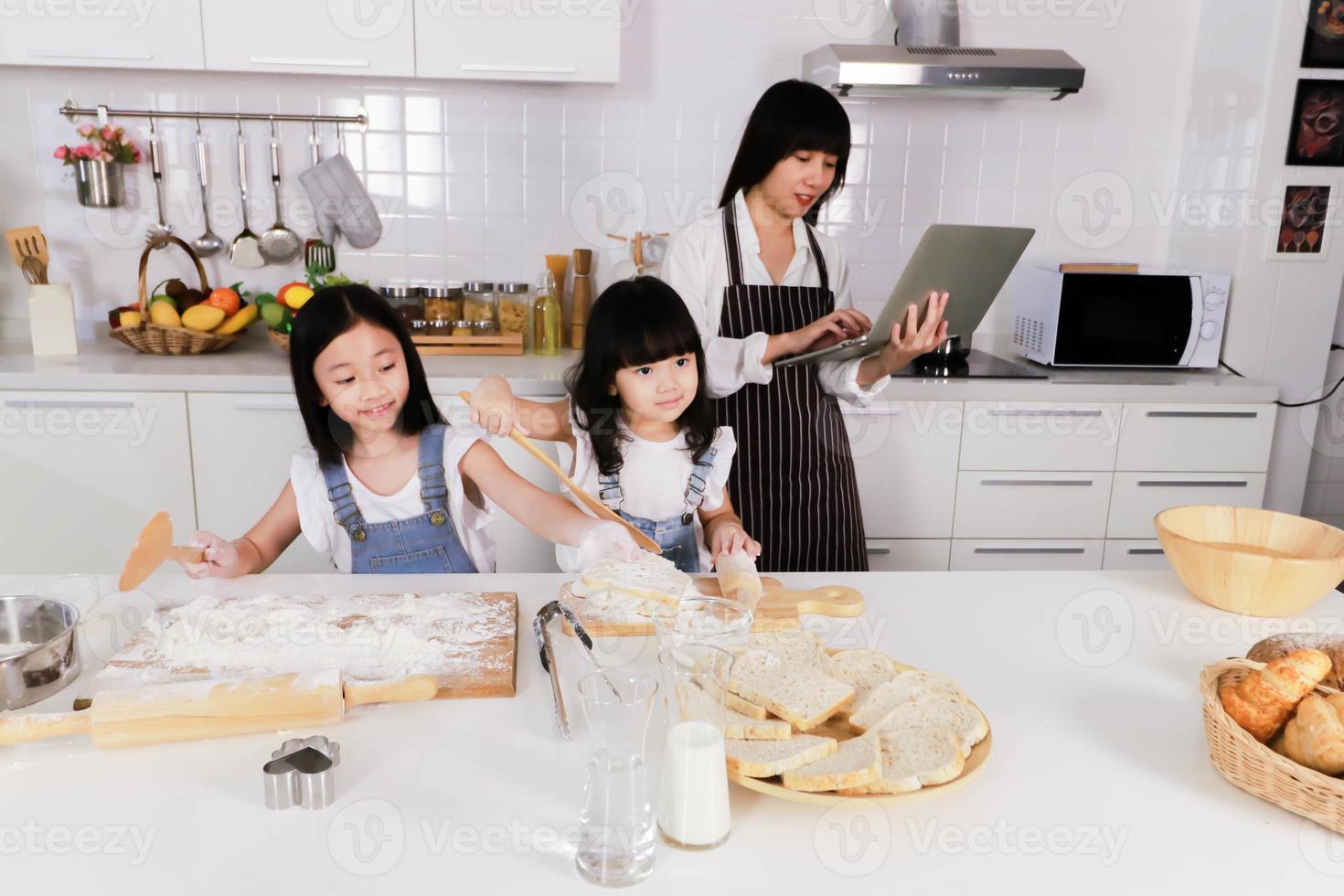 Closeup two daughter make a bake and mother watch notebook photo
