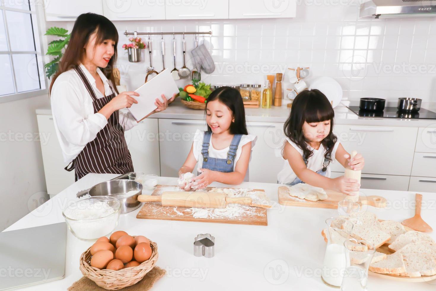 Asian happy family cooking together mom reading a book and two dauther preparing a bake photo