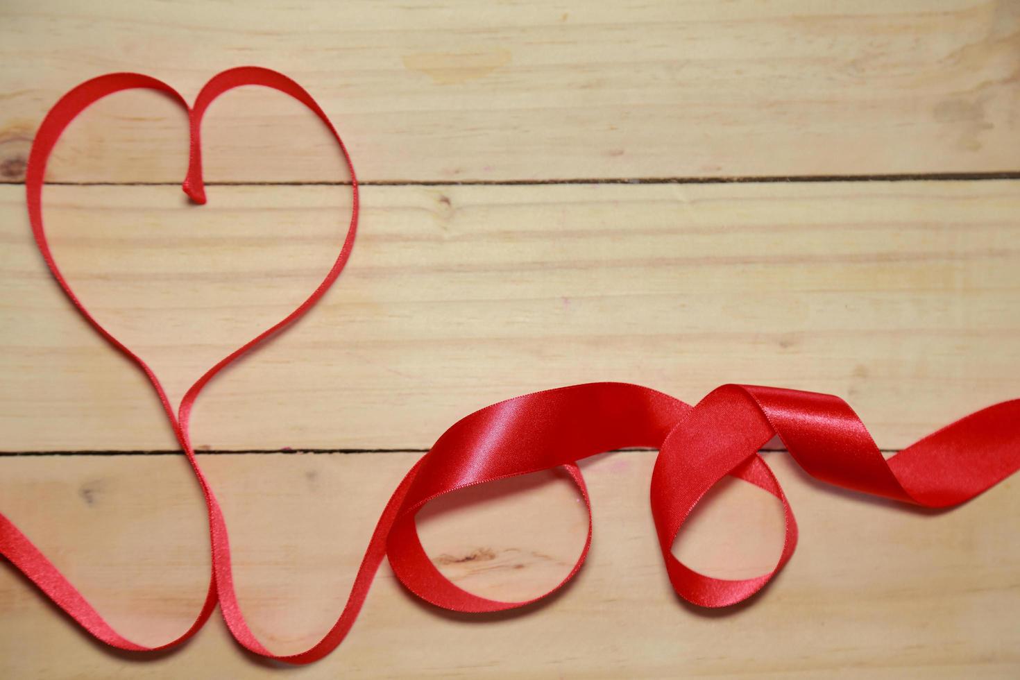 diseñe la conciencia de la cinta en forma de corazón rojo sobre fondo de madera envejecida. concepto de San Valentín. espacio para texto. foto