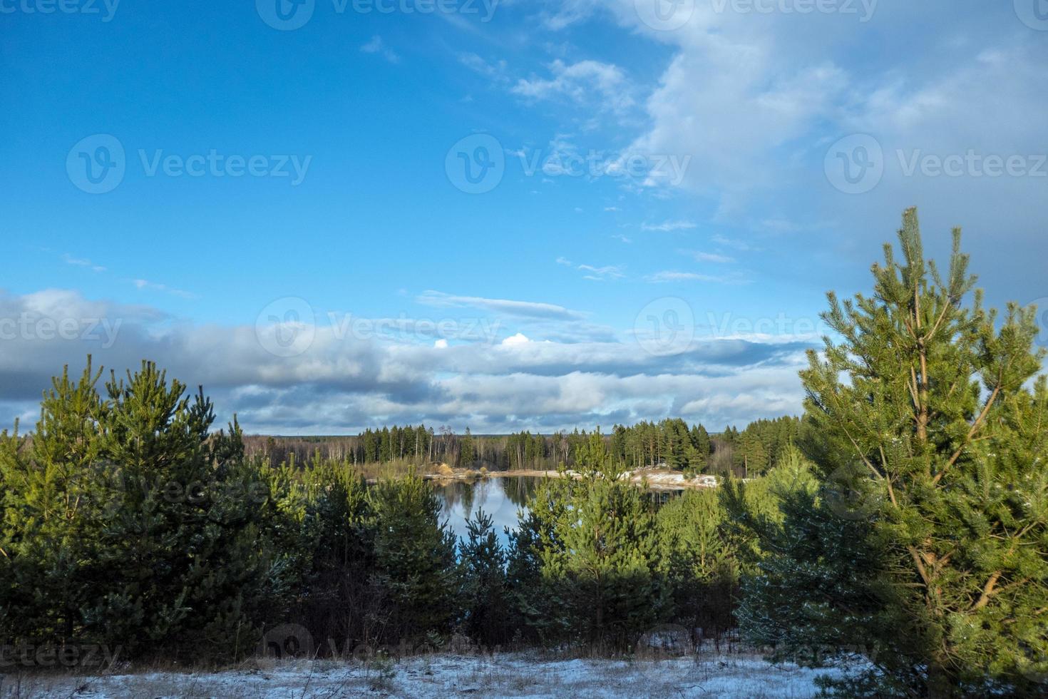 Spring landscape with a beautiful lake with fir trees and last snow against a cloudy sky photo