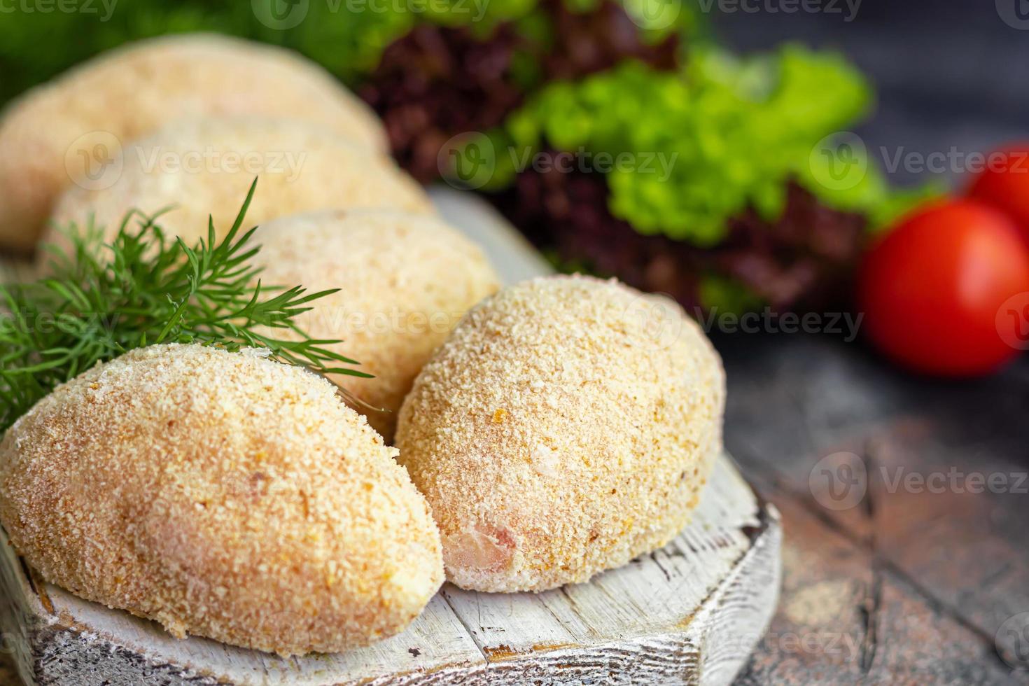 Semi-finished cutlets with breaded cheese or butter. Fast food preparation. On a dark background. photo