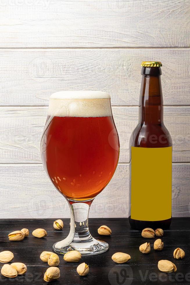Glasses with different types of craft beer on a wooden bar. In glasses and bottles. Nuts and crackers on the table. On a dark background. photo