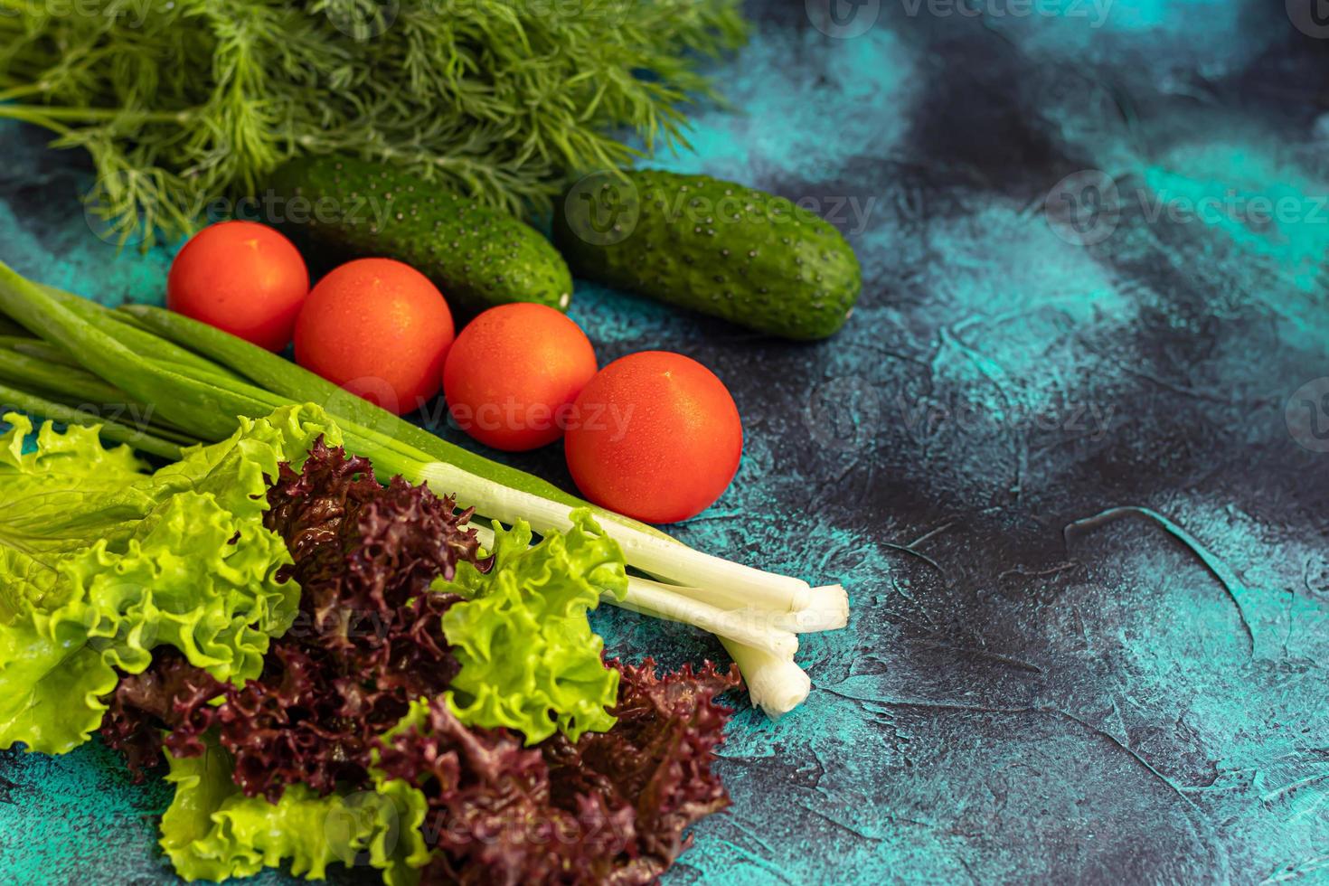 Fresh vegetables for salad. Tomatoes and lettuce, cucumbers with zucchini and cabbage with dill. Spring harvest, benefits and vitamins. On a dark background. photo