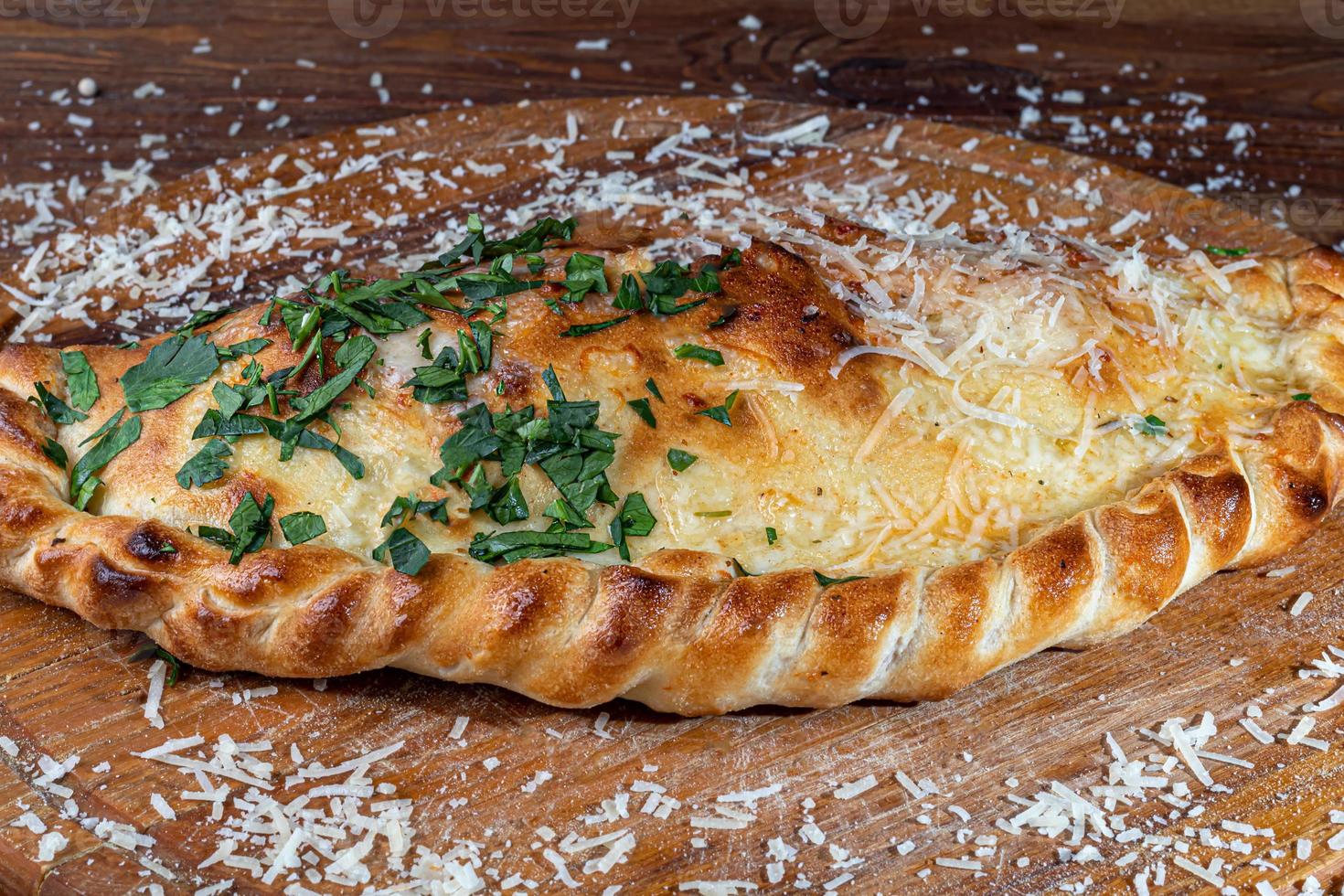 Pizza calzone with bacon and cheese, herbs and cherry tomatoes. With mozzarella, shrimps and octopuses, mussels and other products on a wooden background. photo