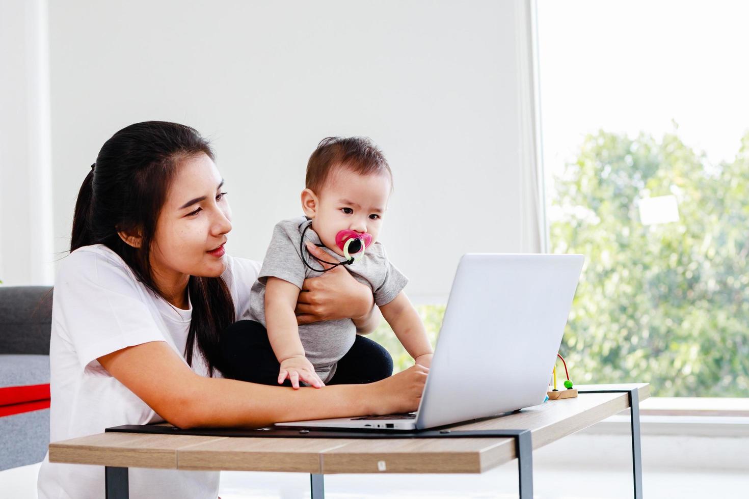 Happy Young Mother with a Child Working at a Computer, Single mom freelancer concept. photo