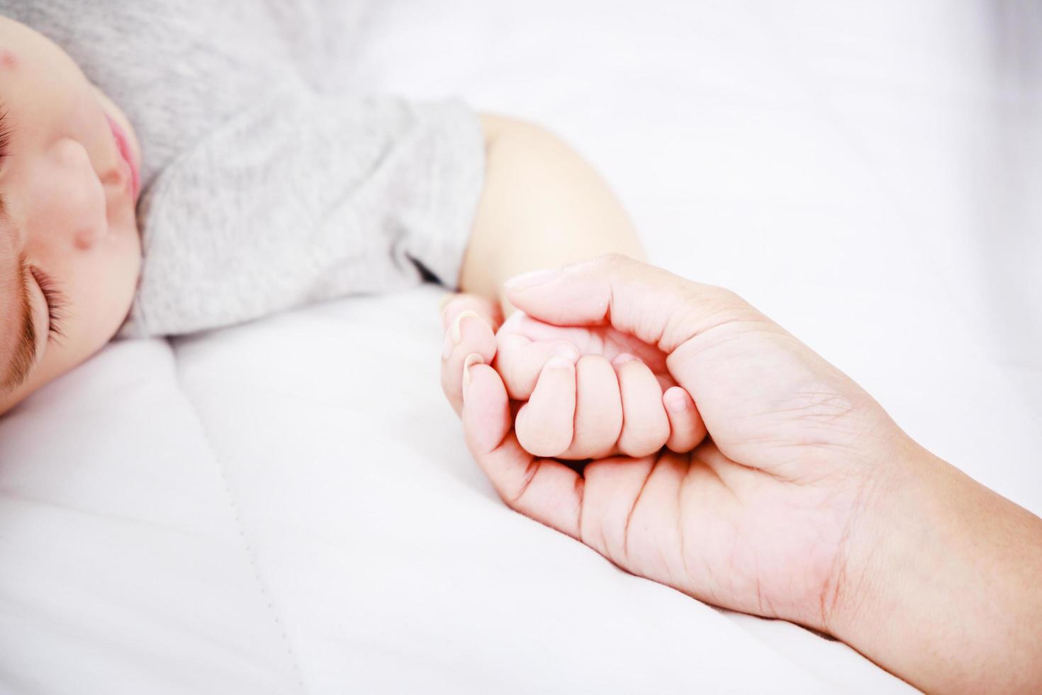 Cerrar por encima de la vista de la madre sosteniendo la mano de su bebé en la cama, familia feliz recién nacido foto