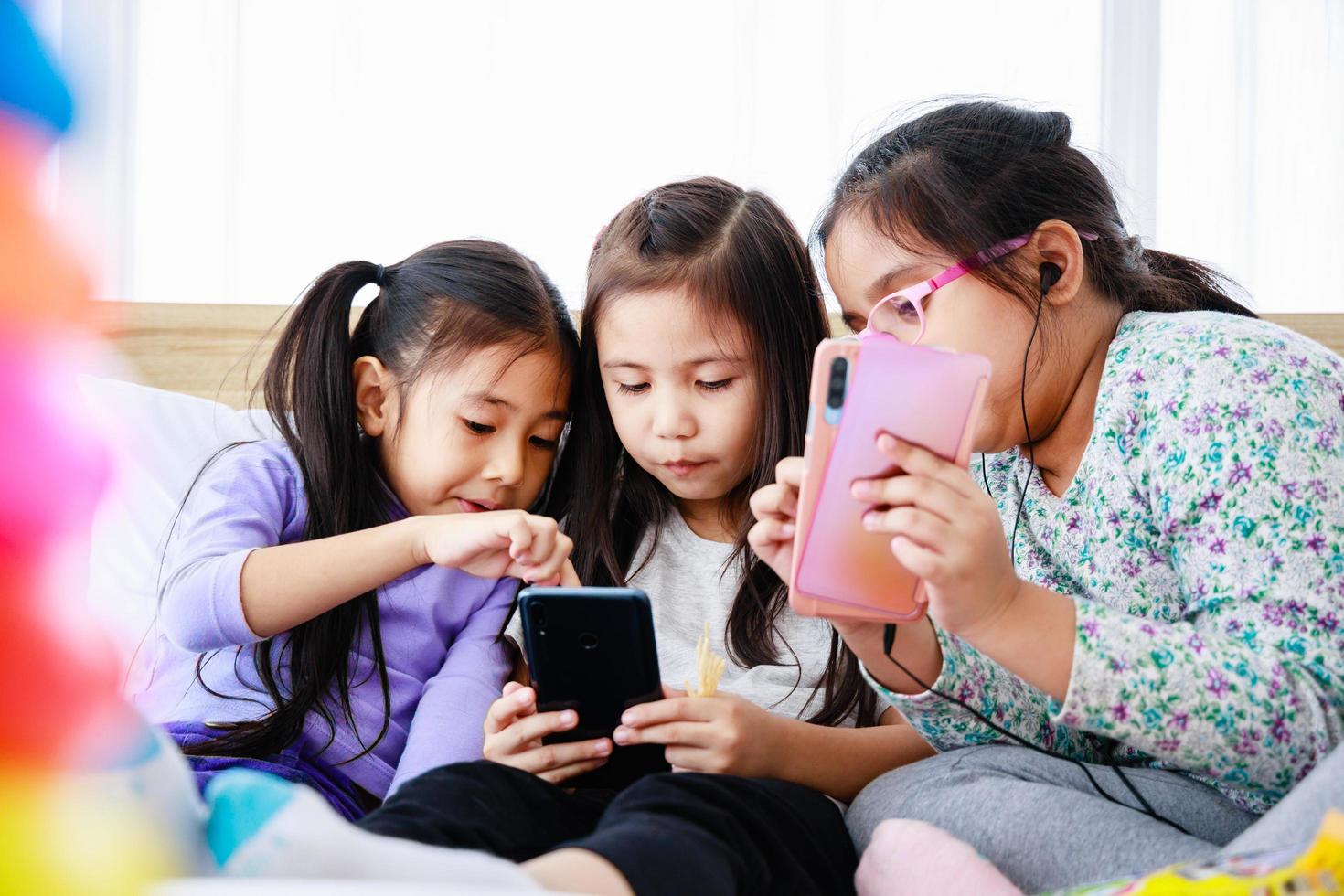 Three Asian cute little girls playing smartphone for playing or studying together at home photo