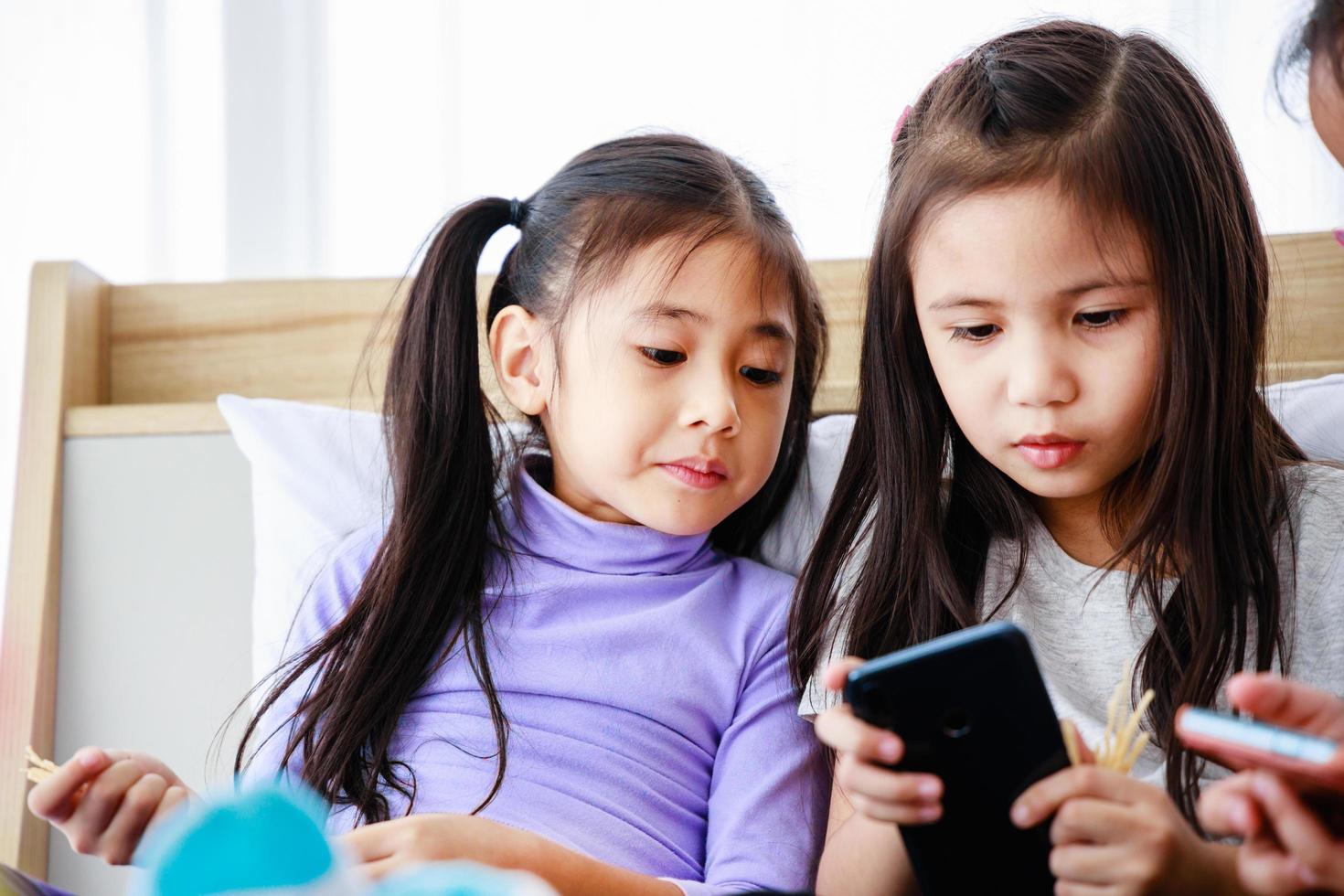 Three happy cute little girls playing smartphone for playing or studying together at home photo