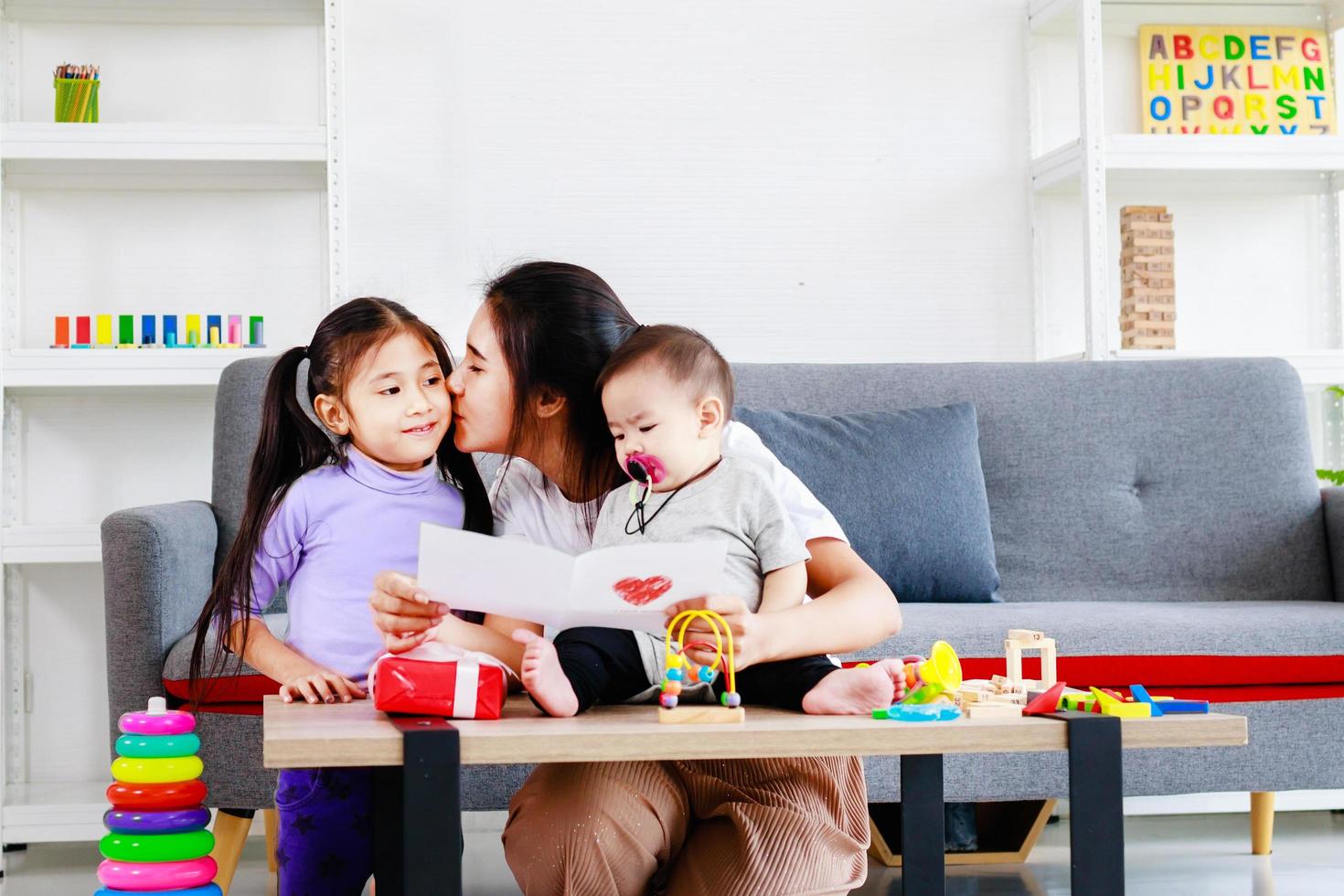 linda hija envía amor regalo de mamá a la madre y besa mientras juega con el bebé, concepto del día de la madre foto