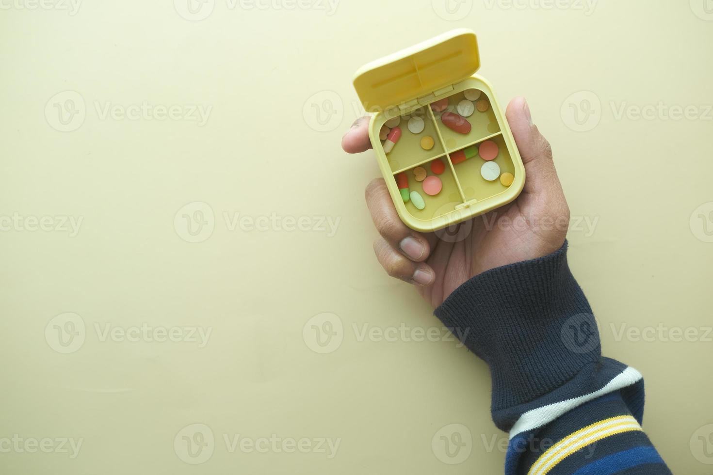 manos del hombre tomando medicamentos de una caja de pastillas con fondo amarillo foto