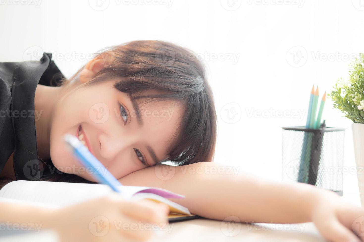 hermosa joven asiática sonrisa y feliz escritura aprendizaje examen o tarea y acostado con escritorio, estilo de vida belleza asia chica con trabajo, educación y concepto de negocios. foto