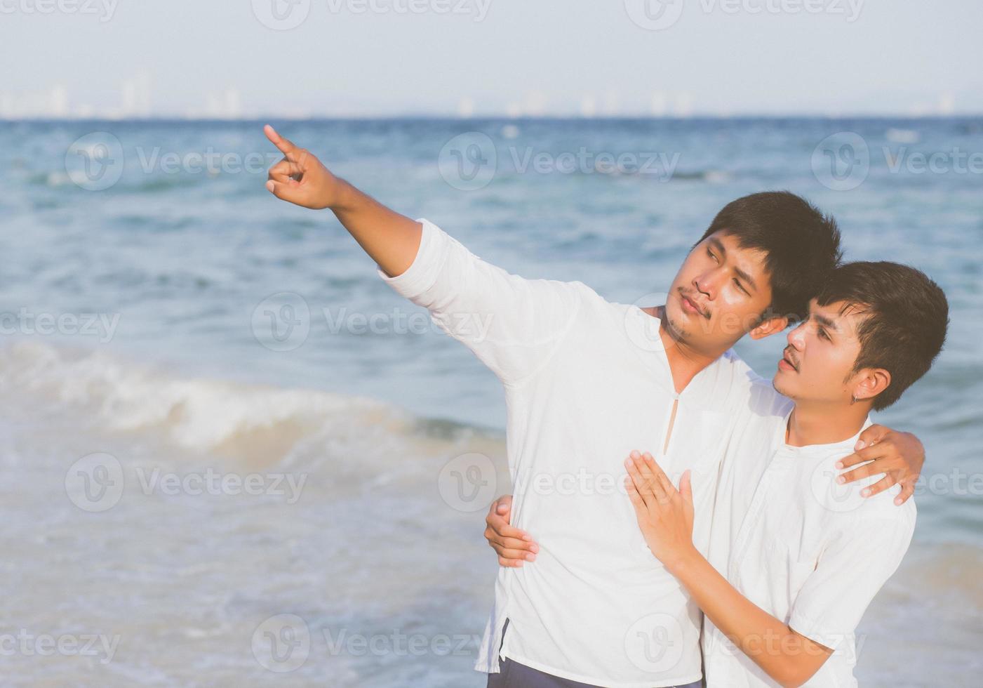 Homosexual portrait young asian couple standing pointing something together on beach in summer, asia gay going sea for leisure with romantic and happy in vacation at sea, LGBT with legal concept. photo