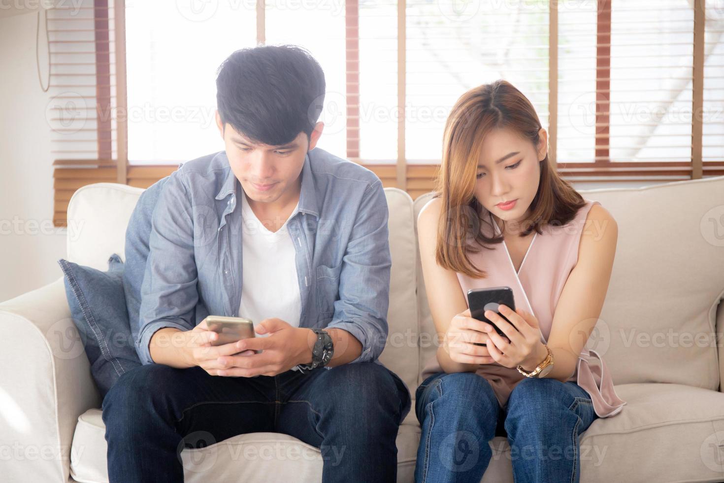 Young asian couple sitting on sofa with problem about relationship because addicts social network media together, asia family expression with looking phone with ignoring and indifferent. photo