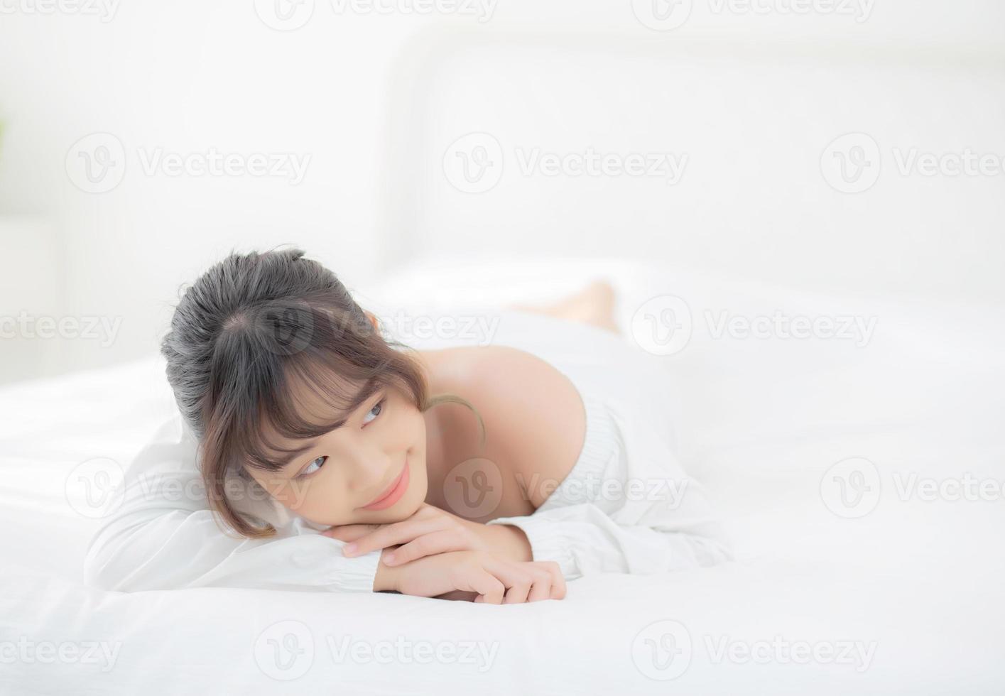 hermoso retrato joven mujer asiática acostada y sonriendo mientras se despierta con el amanecer en la mañana, belleza linda chica feliz y alegre descansando en la cama en el dormitorio, estilo de vida y concepto de relajación. foto