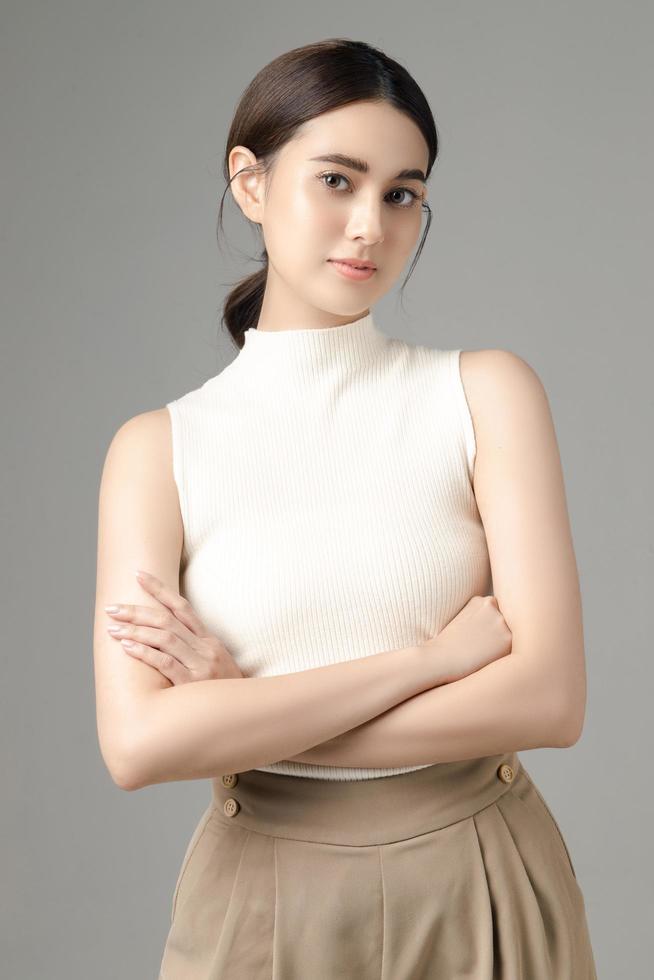 Confident Asian woman crossing her arms and looking at camera isolated on gray background. Portrait of a beautiful girl in the studio. photo