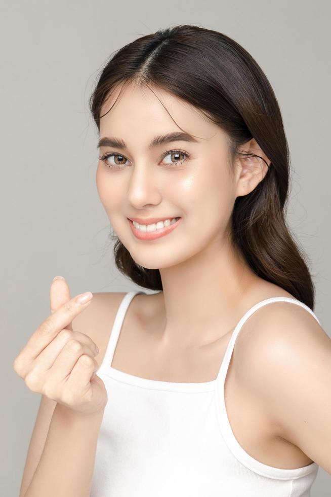 Beautiful young Asian woman model showing heart sign with perfect clean fresh skin on grey background. Face care, Facial treatment, Cosmetology, Plastic Surgery, Lovely girl portrait in studio. photo