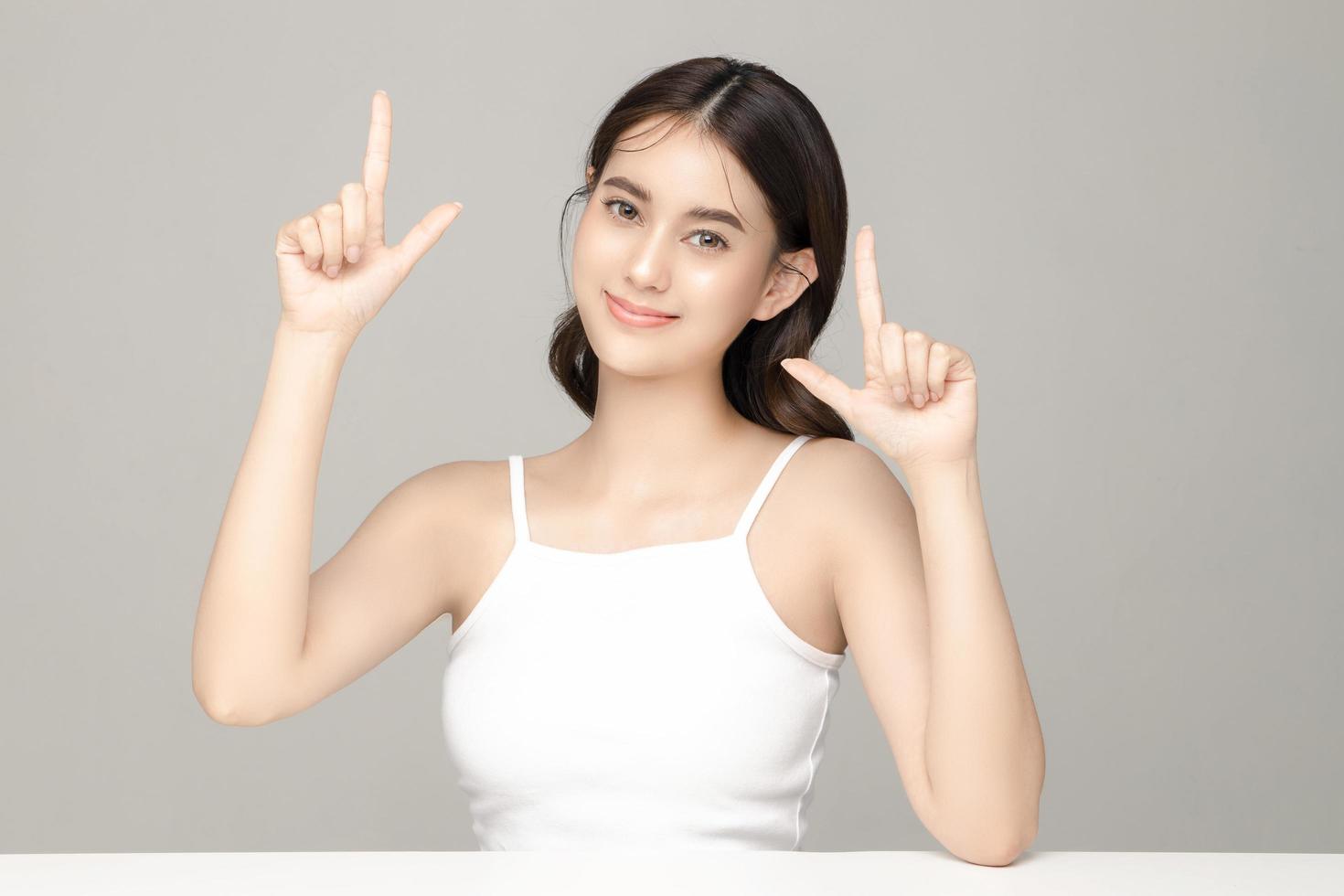 hermosa joven modelo asiática apuntando a copiar espacio con piel limpia y fresca sobre fondo gris. cuidado facial, tratamiento facial, cosmetología, cirugía plástica, hermoso retrato de niña en estudio. foto