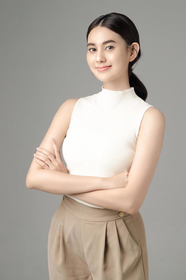 Confident Asian woman crossing her arms and looking at camera isolated on gray background. Portrait of a beautiful girl in the studio. photo