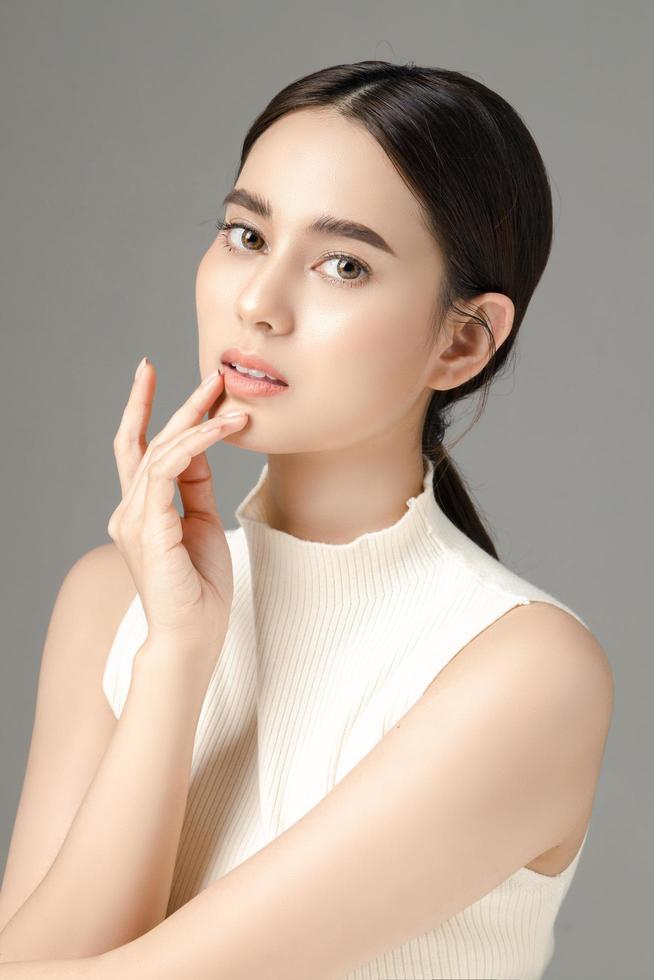 Beautiful young Asian woman model touch her chin with perfect clean fresh skin on grey background. Face care, Facial treatment, Cosmetology, Plastic Surgery, Lovely girl portrait in studio. photo