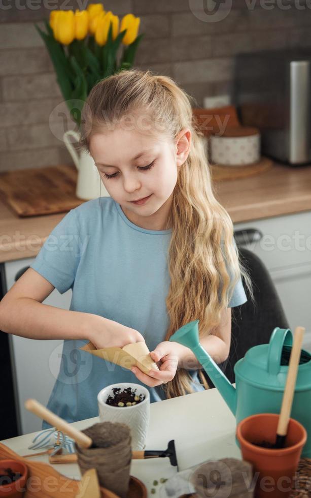 Little girl sitting at the table at home, sowing seeds into flower pots. photo