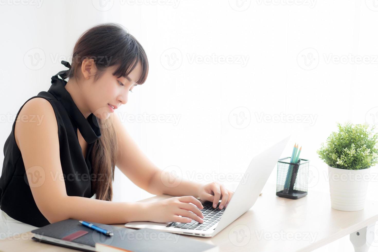 Young freelance asian woman smiling working and typing on laptop computer at desk office with professional, girl using notebook checking email or social network, business and lifestyle concept. photo