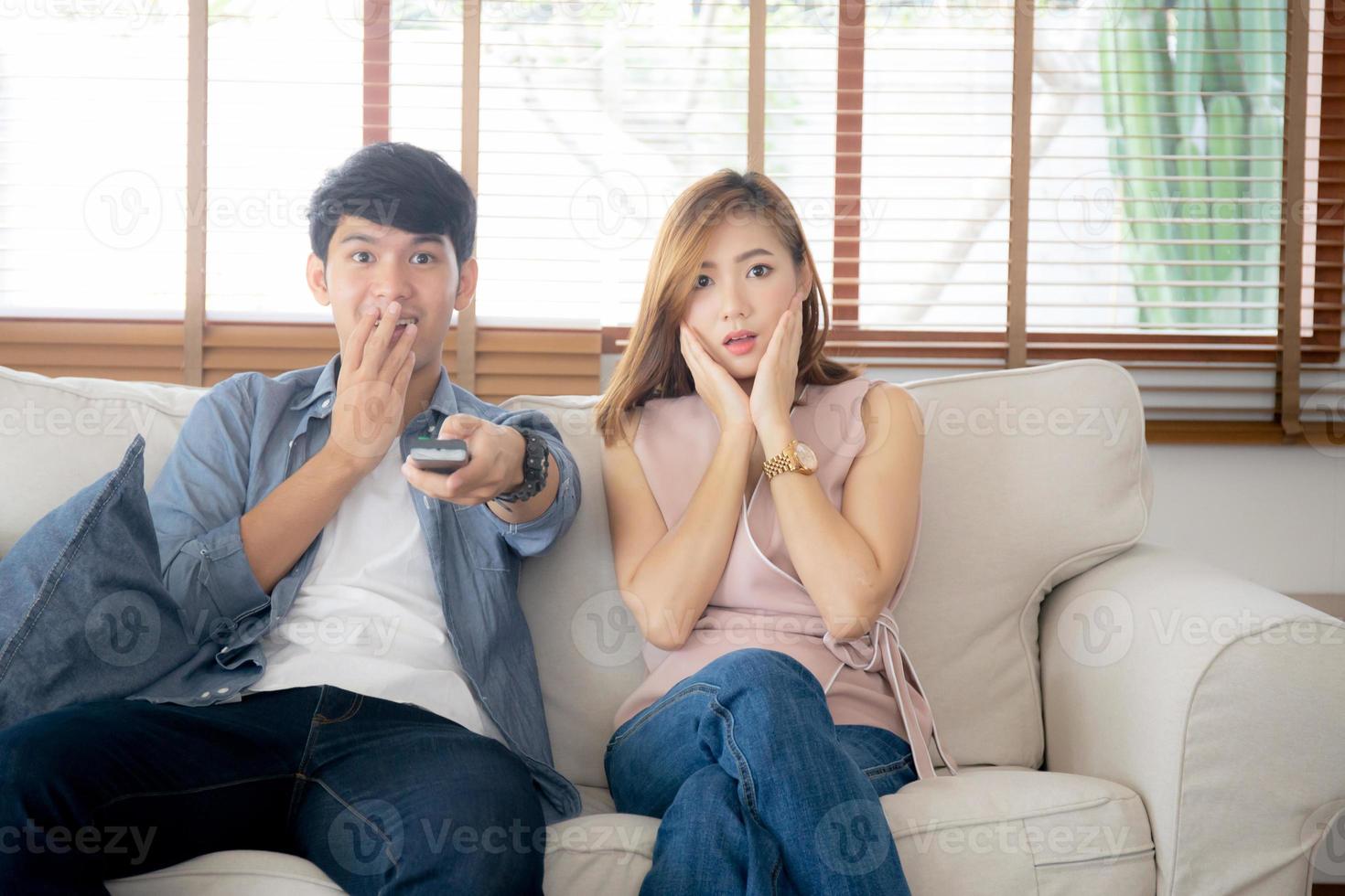 Young asian couple watching horror movie with relax and enjoy holding remote control tv at home, asia man and woman fun surprised and scared together at home, entertainment concept. photo