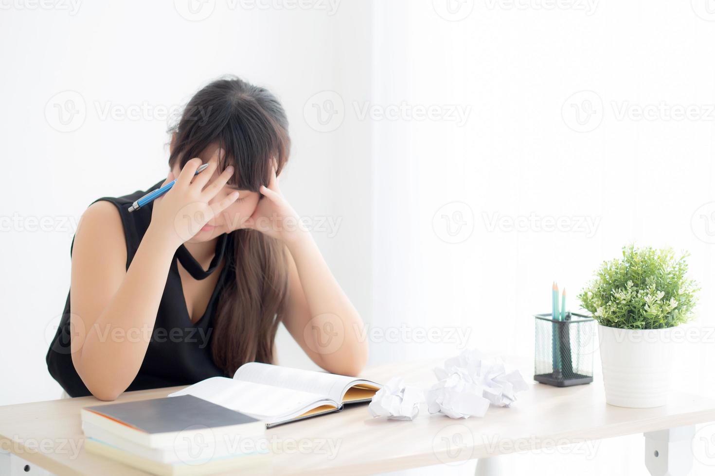 hermosa mujer asiática cansada y estresada por escribir con exceso de trabajo en el escritorio, chica preocupada sin idea con cuaderno y papel arrugado en la oficina, concepto independiente y de negocios. foto
