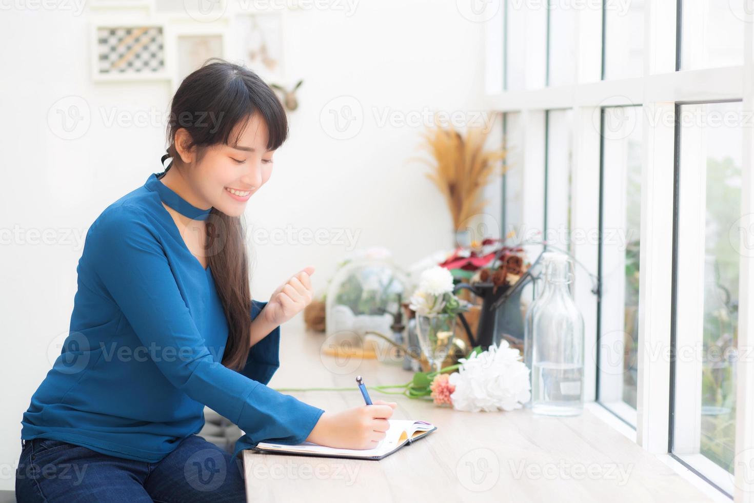 Beautiful portrait asian woman writer excited writing on notebook or diary with happy with success and glad, lifestyle asia girl is student, female plan working, education and business concept. photo