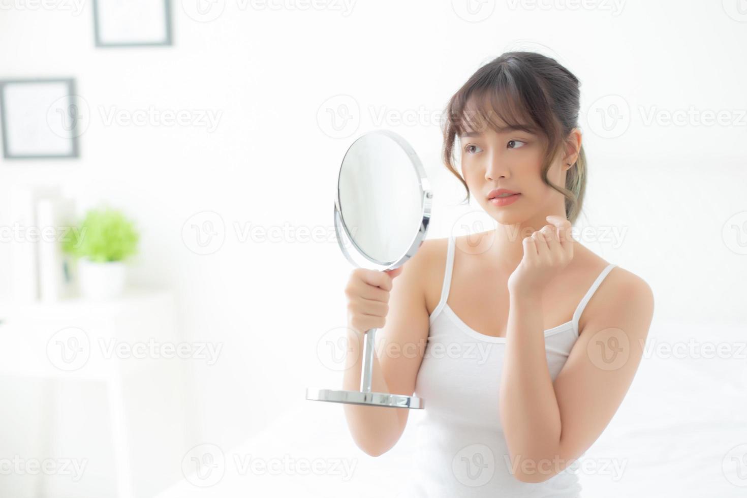 Beautiful young asian woman looking the mirror with acne problem at bedroom, trouble of beauty on face, zit treatment, asia girl is pimple having worry and displeased, skincare and healthy concept. photo