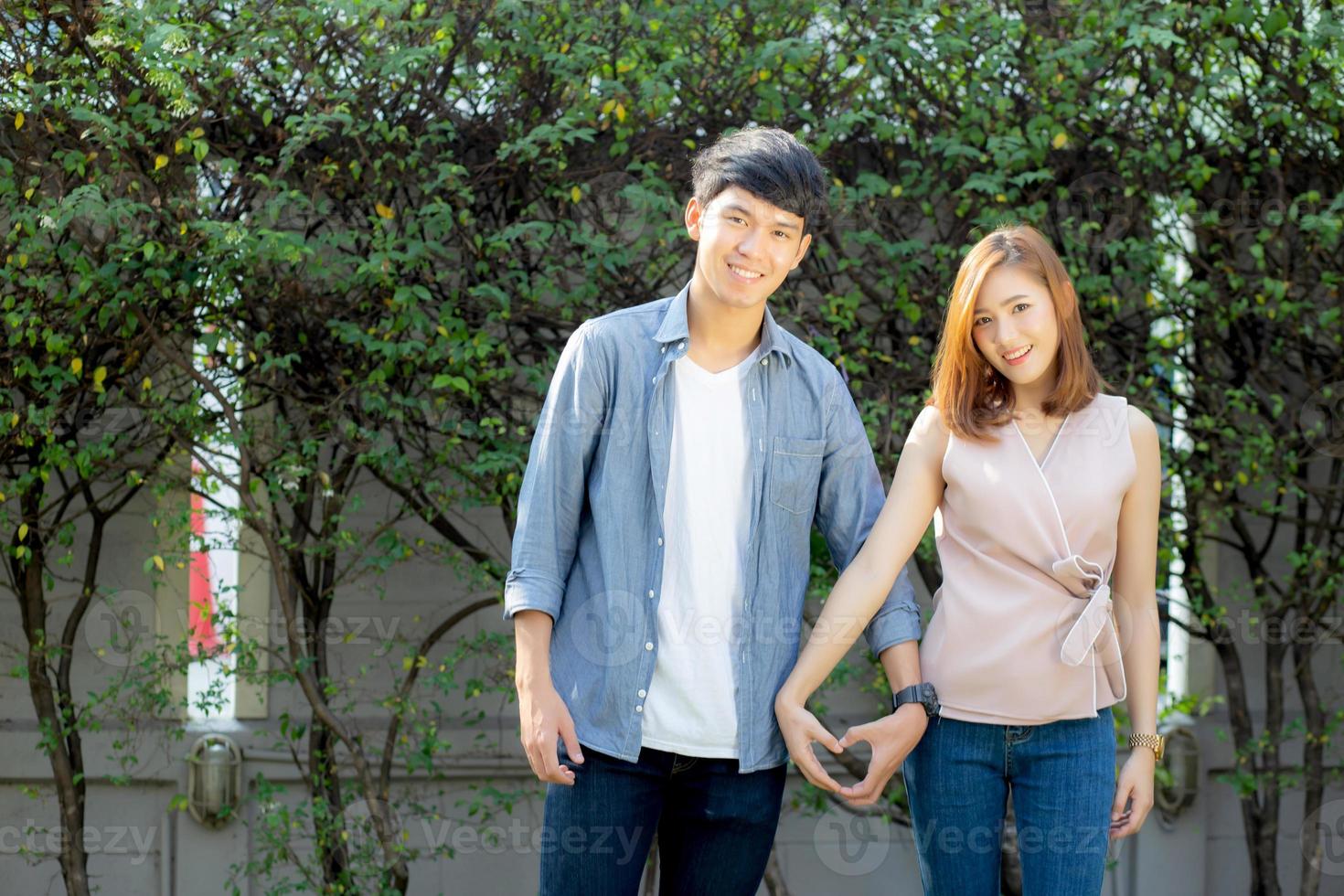 Beautiful happy young couple fun making gesture heart shape with hand outdoor together, man and woman with relation feeling love with symbol and sign in the garden, lover and romantic concept. photo