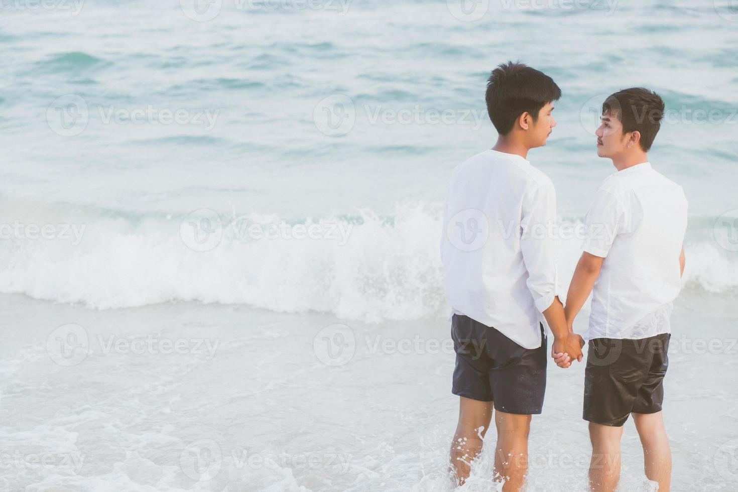 vista posterior joven pareja asiática de pie juntos en la playa en verano, asia gay tomados de la mano yendo al mar por placer y relajarse con romántico y feliz en vacaciones en el mar, lgbt con concepto legal. foto