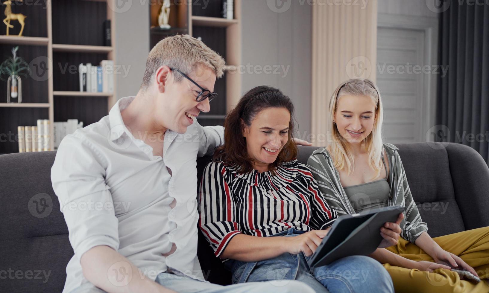 familia caucásica feliz usando tableta, computadora portátil, teléfono para jugar, ver películas, relajarse en casa para el concepto de estilo de vida tecnológico foto