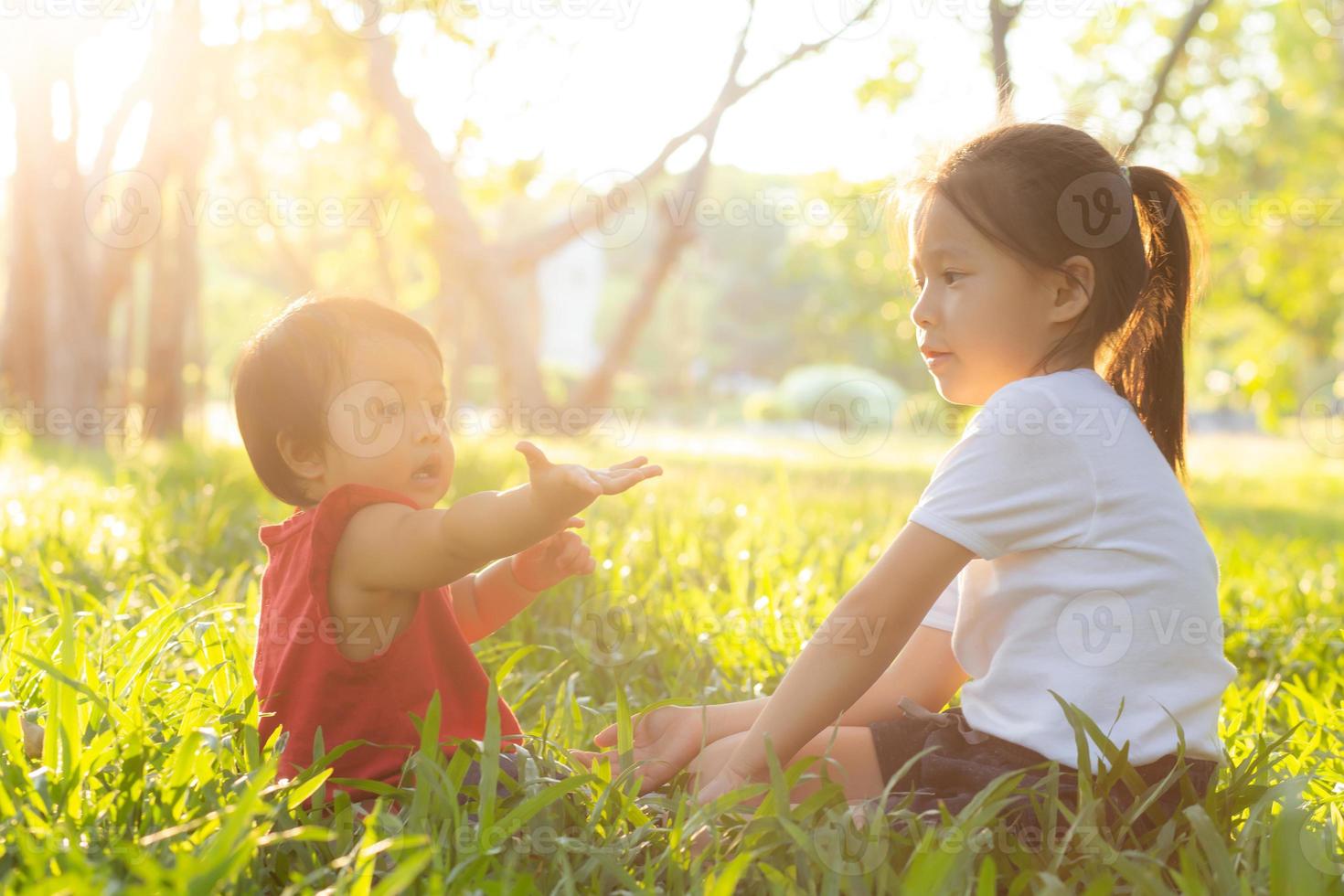 hermoso niño asiático joven sentado jugando en verano en el parque con disfrute y alegre en la hierba verde, actividad infantil con relajación y felicidad juntos en el concepto de pradera, familia y vacaciones. foto